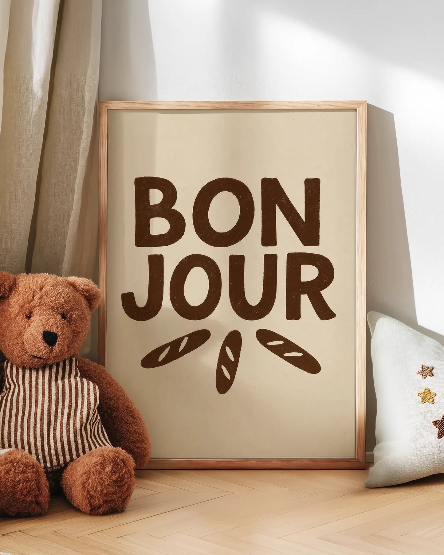 Barntavla med texten "BON JOUR" i bruna bokstäver och små baguetter lutad mot vägg bredvid nalle. En mysig och humoristisk väggdekoration i barnrummet.