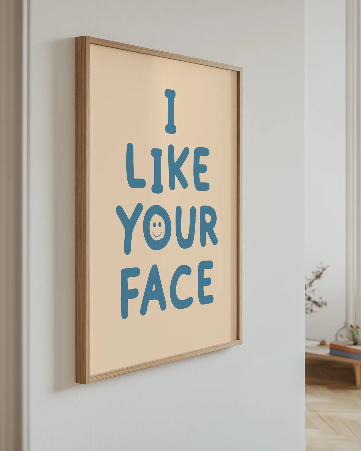 Barntavla med blå text “I LIKE YOUR FACE” på beige bakgrund upphängd på vägg med ekram. En modern och lekfull väggdekoration.