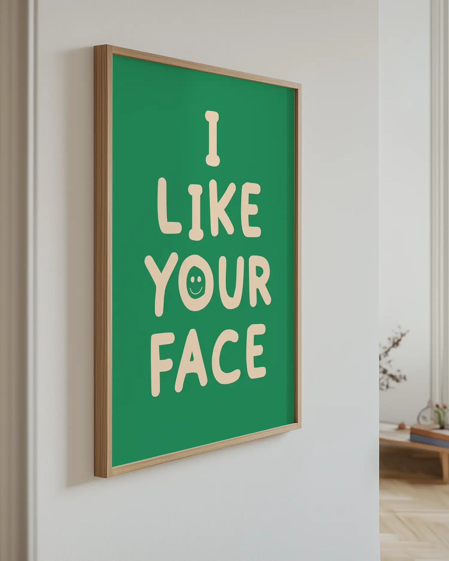 Barntavla med texten “I LIKE YOUR FACE” i beige på grön bakgrund upphängd på vägg med ekram. En lekfull och kärleksfull dekoration.
