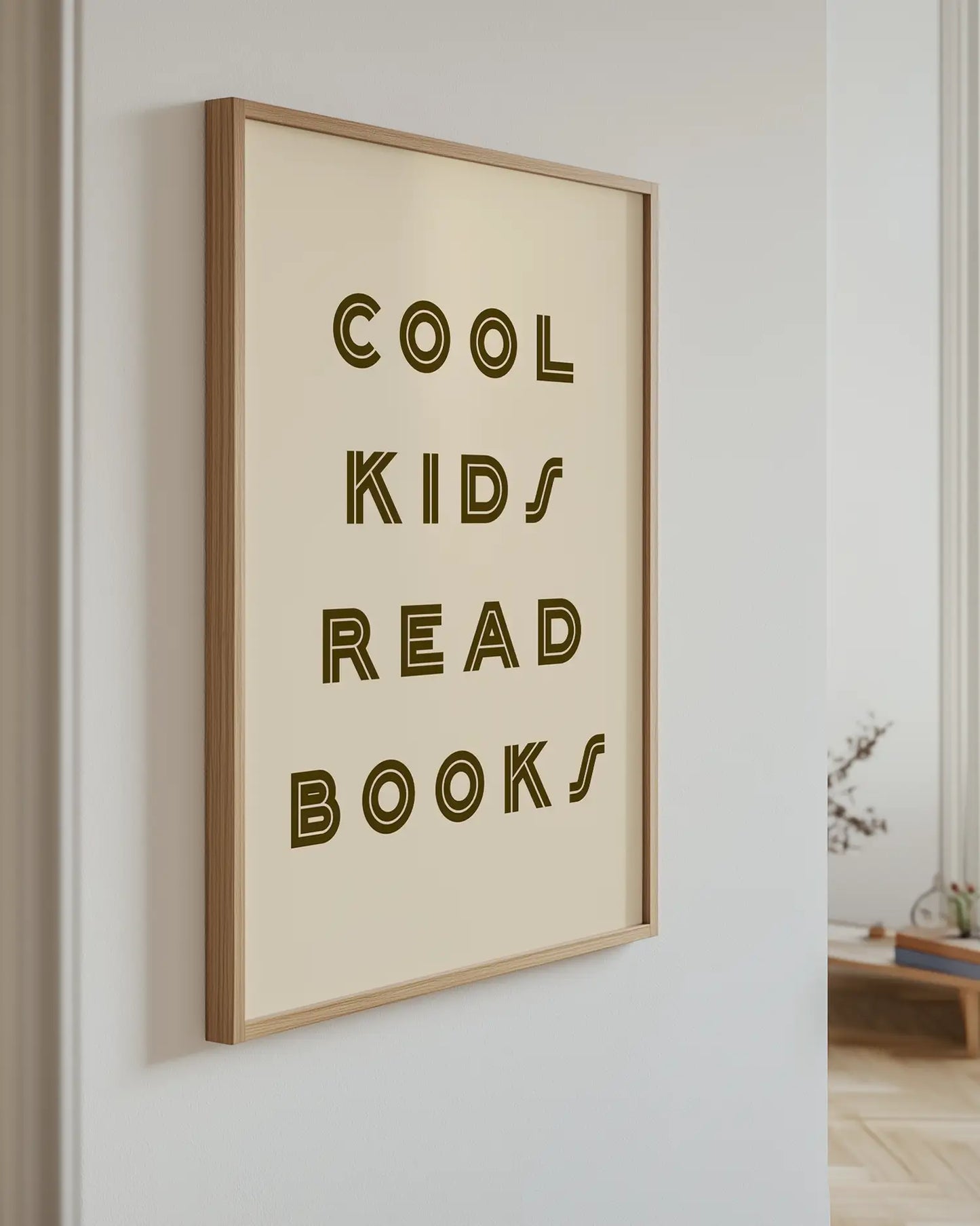 Barntavla med texten "COOL KIDS READ BOOKS" i mörkbrun text på beige bakgrund, upphängd på vägg med ekram. En elegant och positiv detalj som tillför värme.
