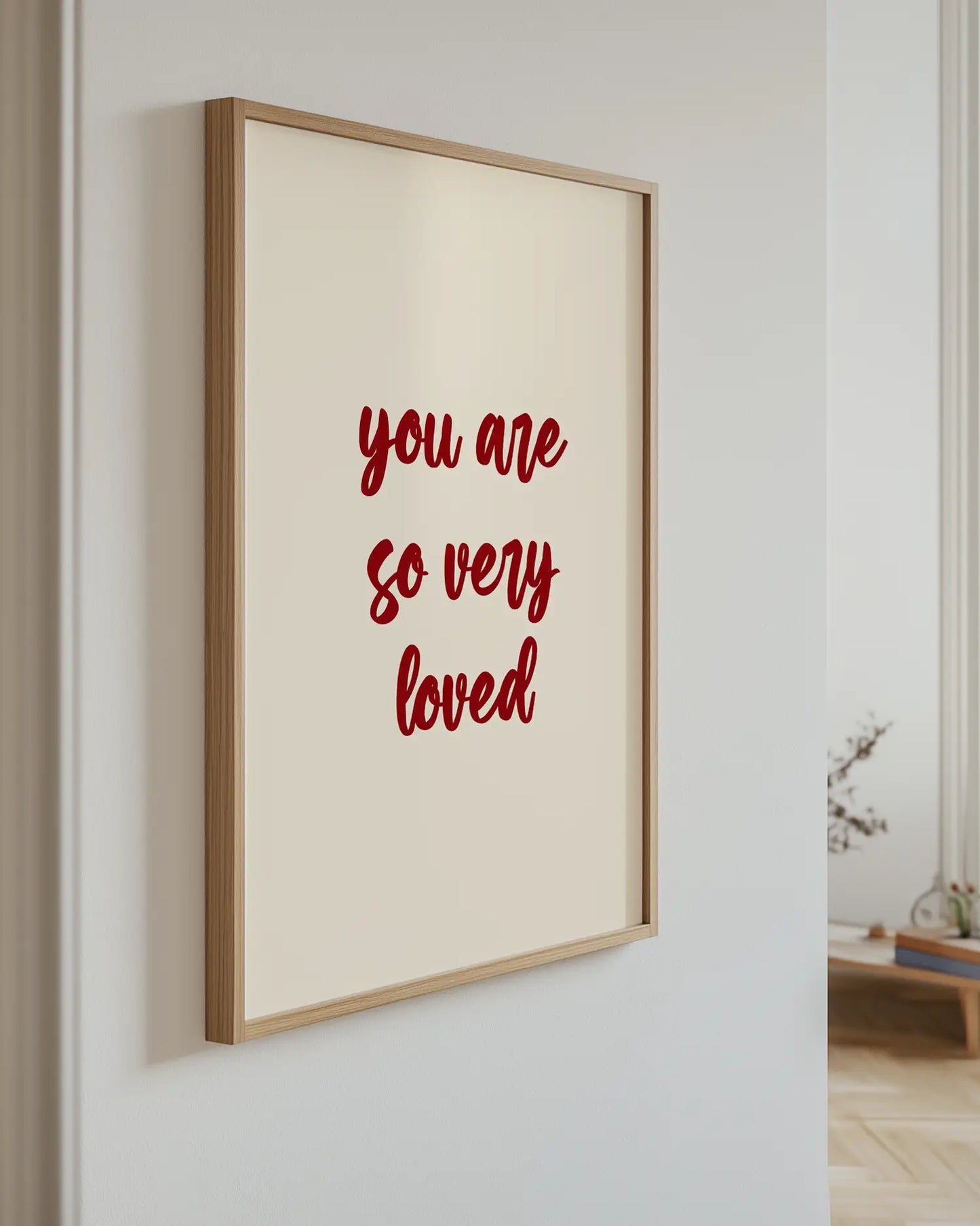 Barntavla med texten "you are so very loved" i mörkröd text på beige bakgrund, upphängd på vägg med ekram. En harmonisk och kärleksfull detalj.