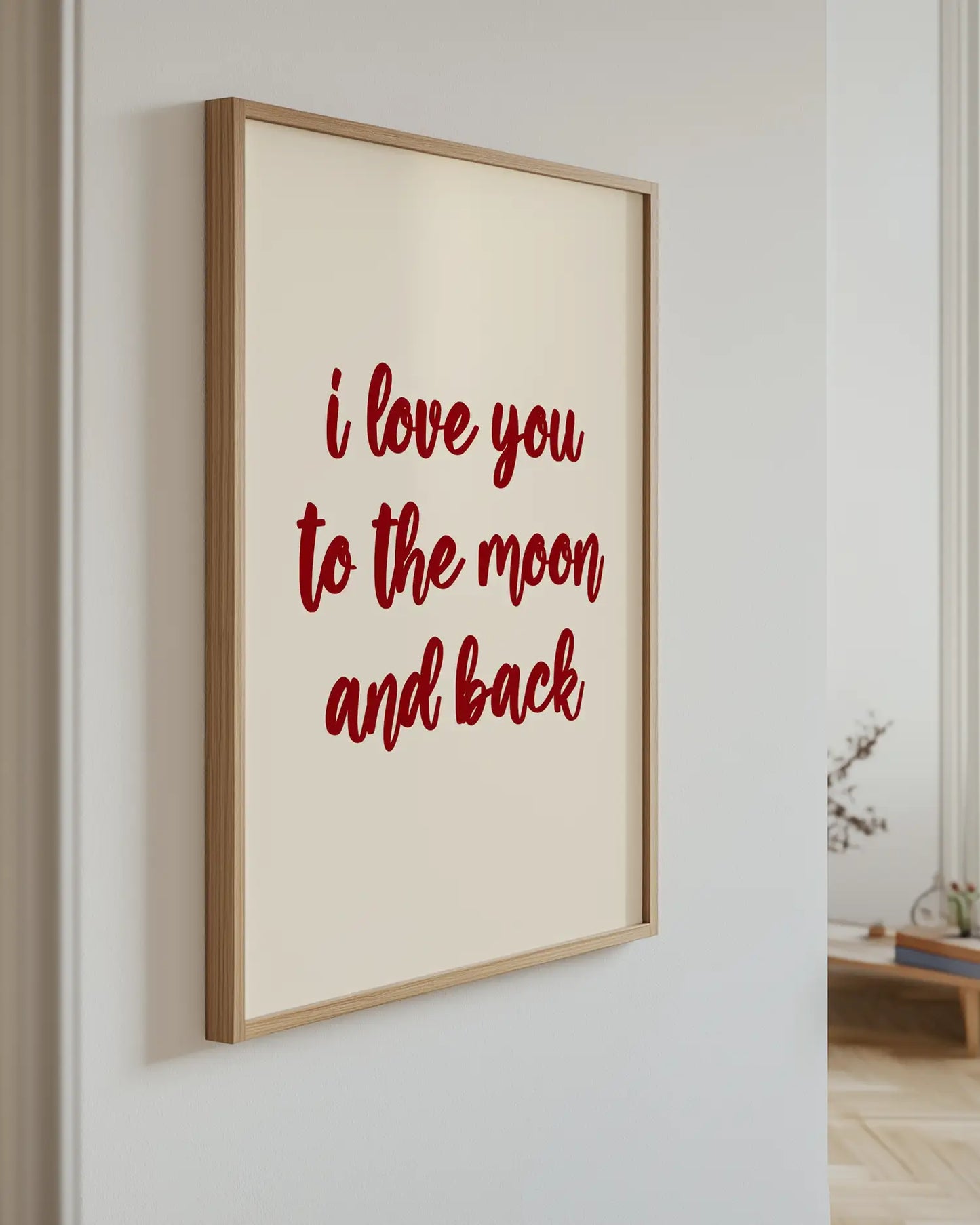 Barntavla med texten "I love you to the moon and back" i mörkröd text på beige bakgrund, upphängd på vägg med ekram. En harmonisk och varm detalj.