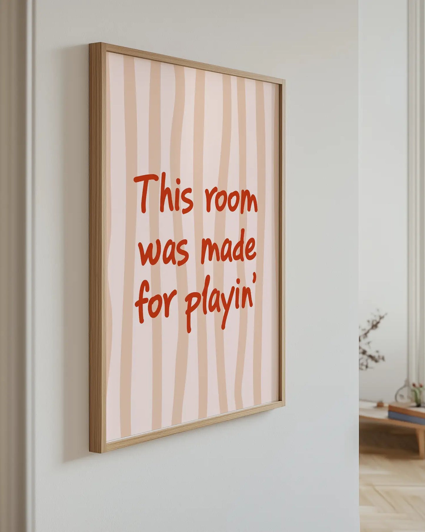 Barntavla med texten "This room was made for playin’" i rött mot ljusrandig bakgrund, upphängd på vägg med ekram. En stilfull och varm detalj i barnrummet.