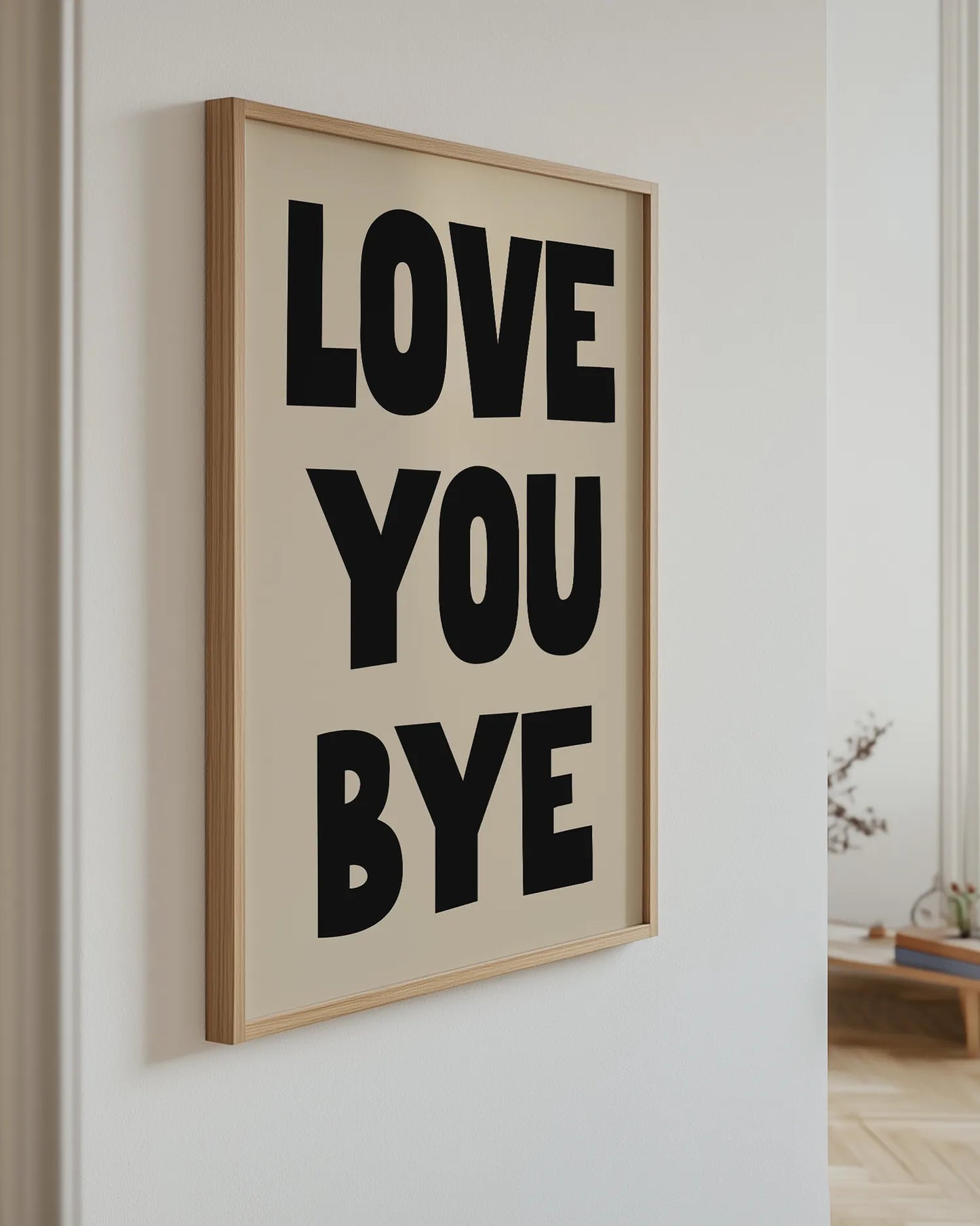 "Love You Bye"-poster i ekram hängande på en ljus vägg i ett modernt hem. Den grafiska textpostern med svart text på beige bakgrund tillför både värme och personlighet till barnrum eller vardagsrum.