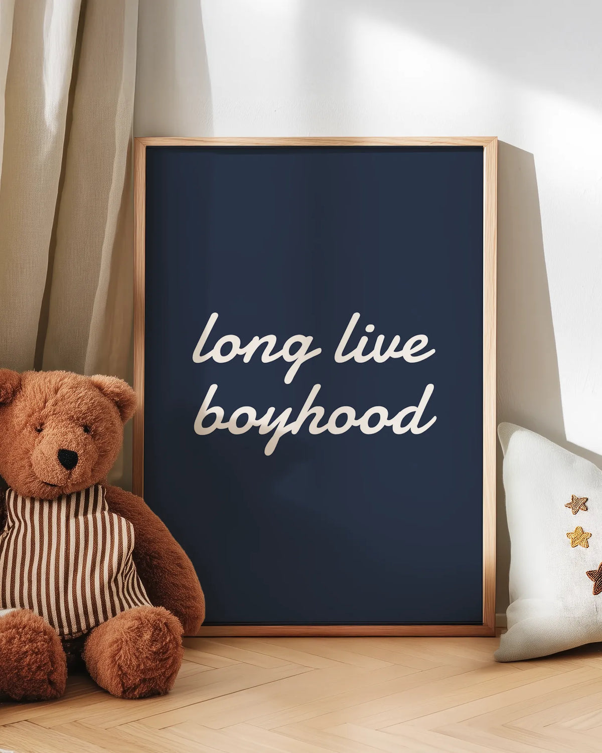 Inramad "Long live boyhood"-poster i ekram stående på golvet bredvid en nallebjörn och kudde i ett barnrum med ljusa gardiner. Den blå bakgrunden och vita texten ger en lugn och klassisk känsla, perfekt för pojkrum i skandinavisk stil.