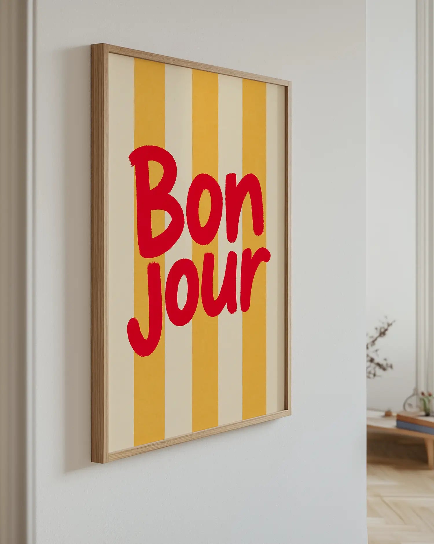 Inramad barntavla med "BON JOUR" i rött och gulrandig bakgrund, hängande på väggen i ljust barnrum. En solig och välkomnande detalj.