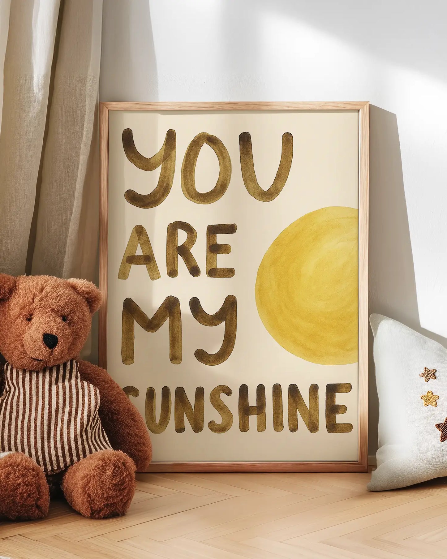 Barntavla med texten "YOU ARE MY SUNSHINE" och gul sol, lutad mot vägg bredvid en nalle. En mysig och kärleksfull väggdetalj för barnrummet.