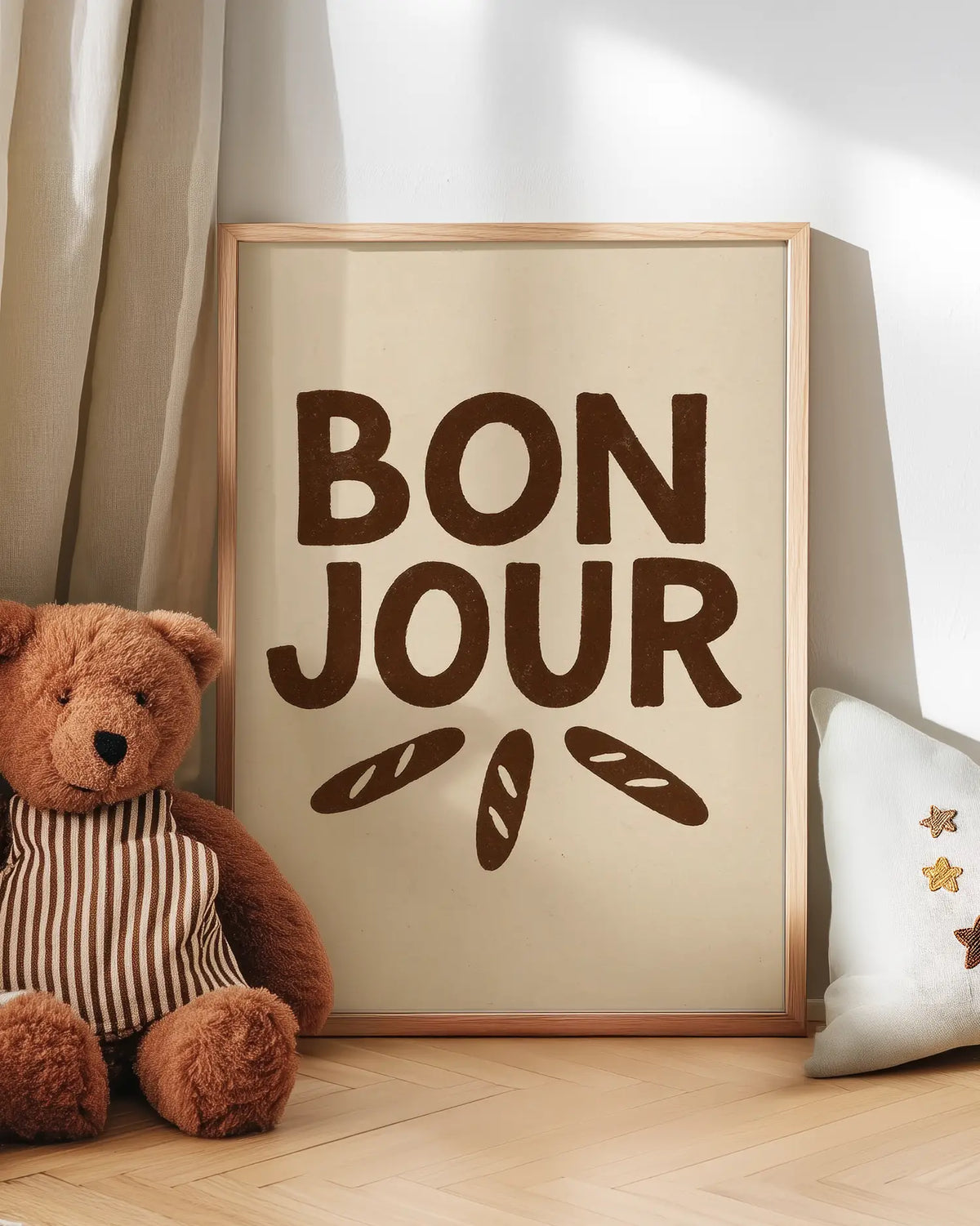 Barntavla med texten "BON JOUR" i bruna bokstäver och små baguetter lutad mot vägg bredvid nalle. En mysig och humoristisk väggdekoration i barnrummet.