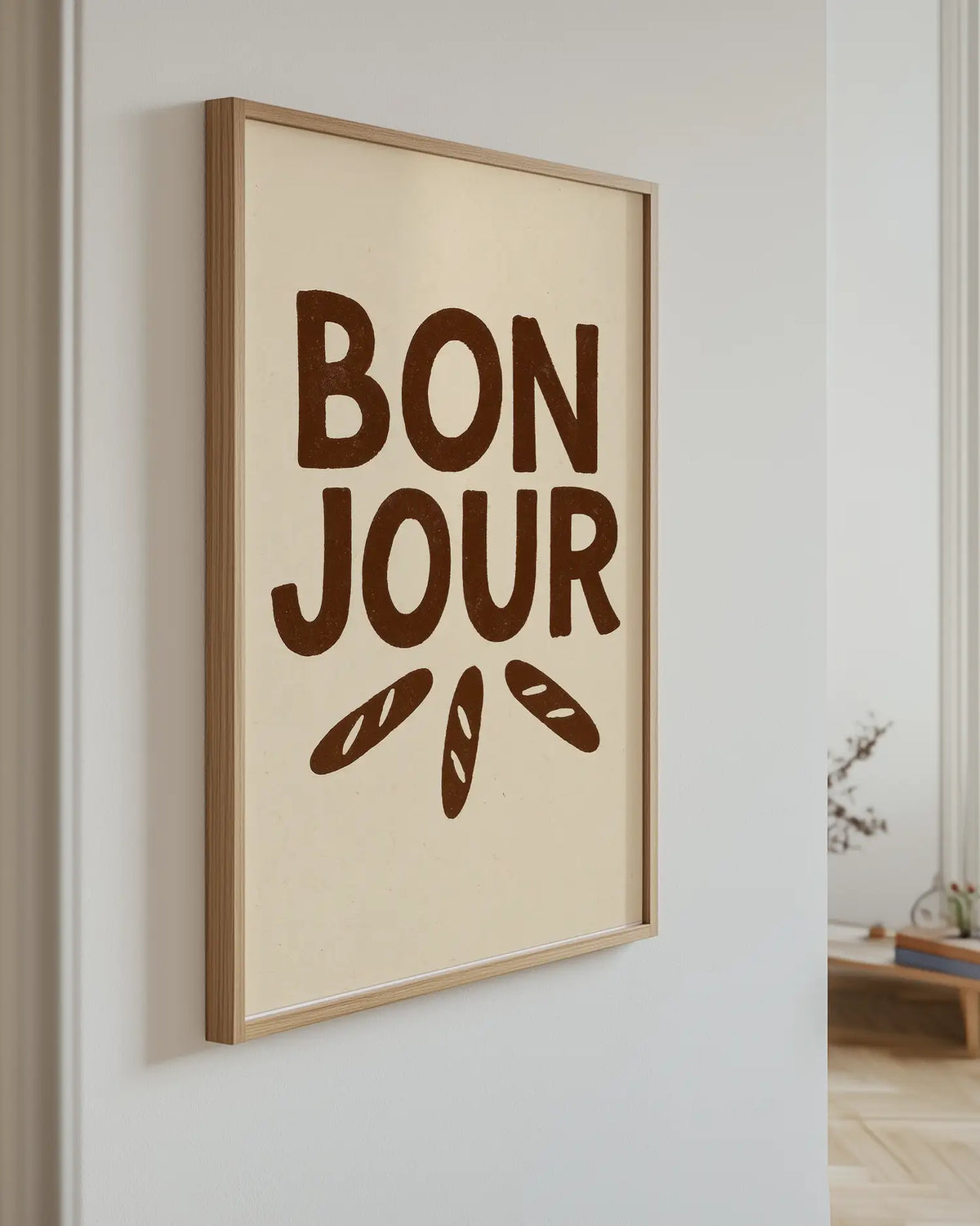 Barnrumstavla med texten "BON JOUR" och baguetteillustrationer upphängd på vägg i ekram. En charmig detalj med frukostkänsla.