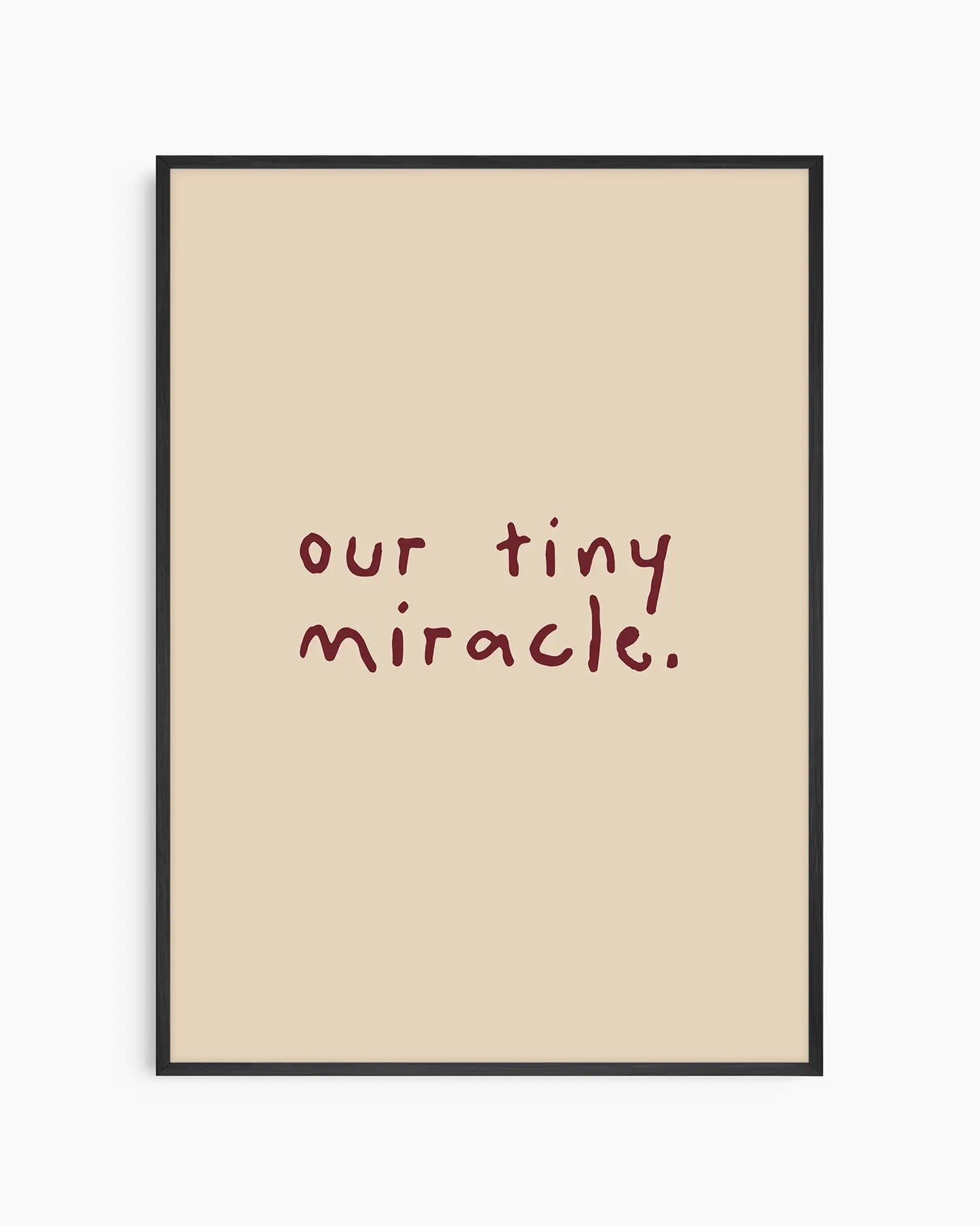 Barntavla med texten "our tiny miracle." i vinröd handskriven stil på beige bakgrund, inramad i svart träram. En mjuk och varm väggdekoration för barnrummet.