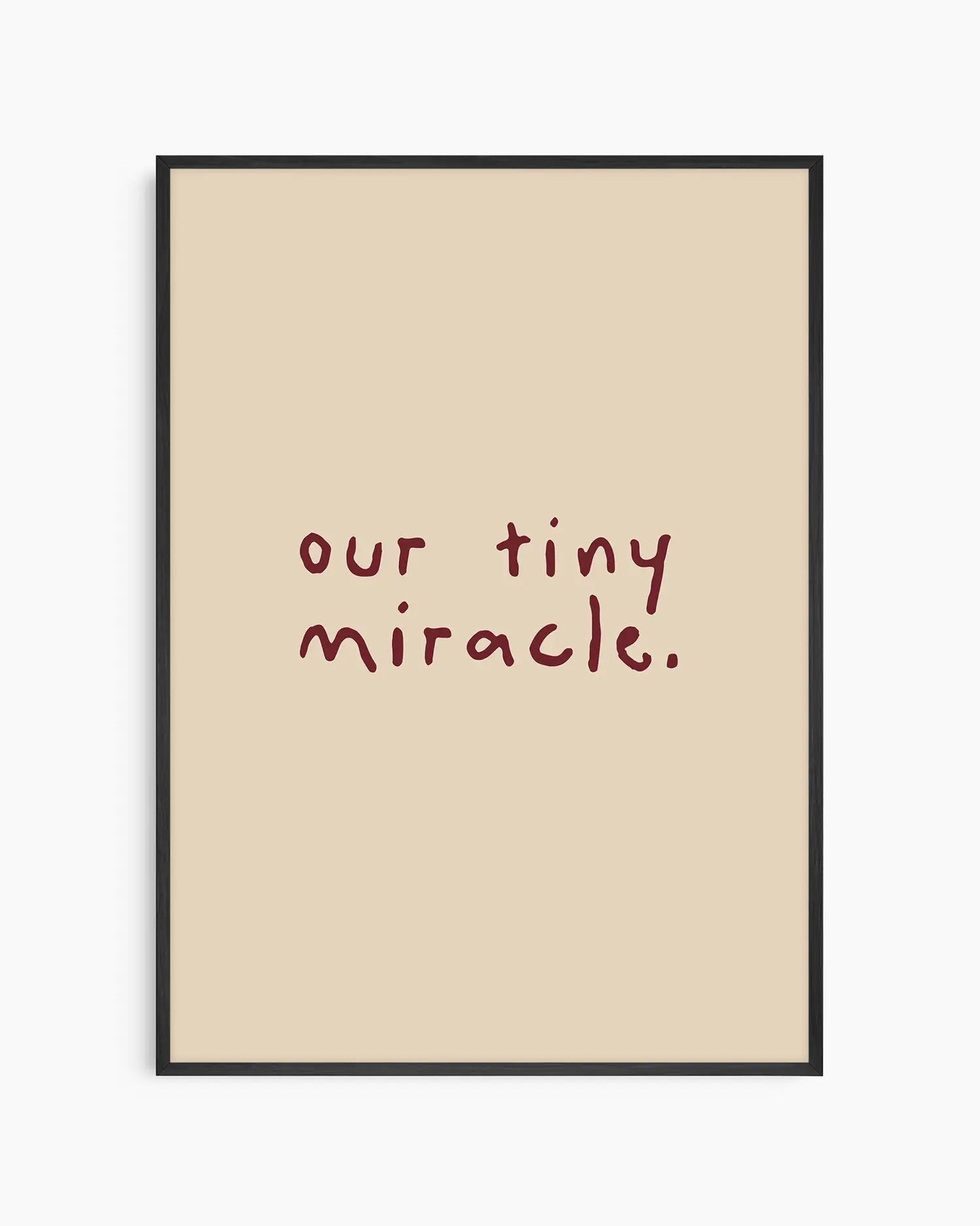 Barntavla med texten "our tiny miracle." i vinröd handskriven stil på beige bakgrund, inramad i svart träram. En mjuk och varm väggdekoration för barnrummet.