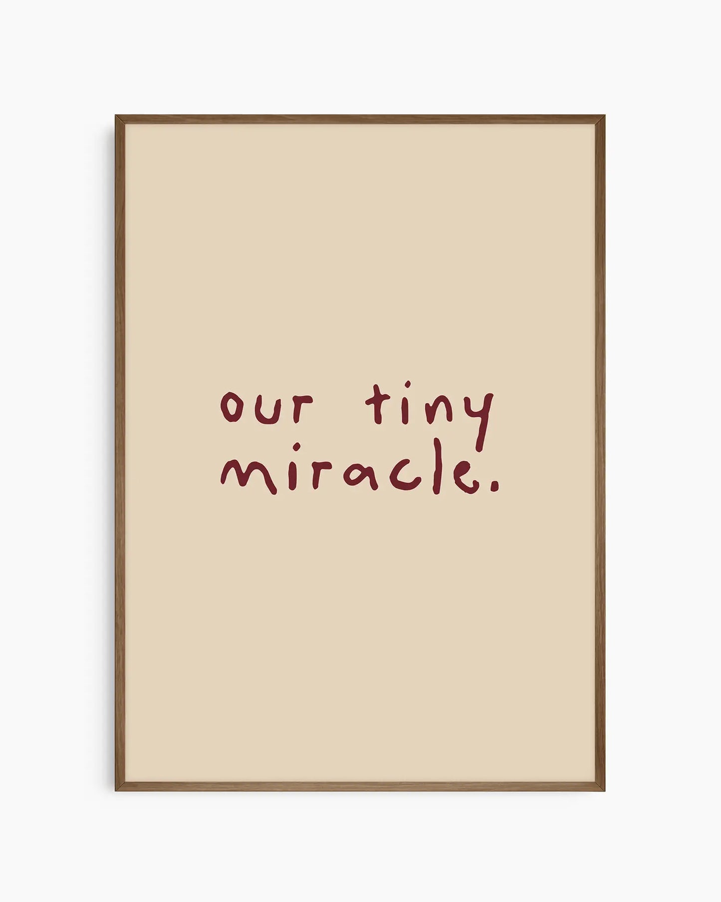 Barnrumstavla med orden "our tiny miracle." i vinröd handskriven typografi på beige bakgrund, inramad i en mörk ekram. En harmonisk och tidlös detalj till barnrummet.