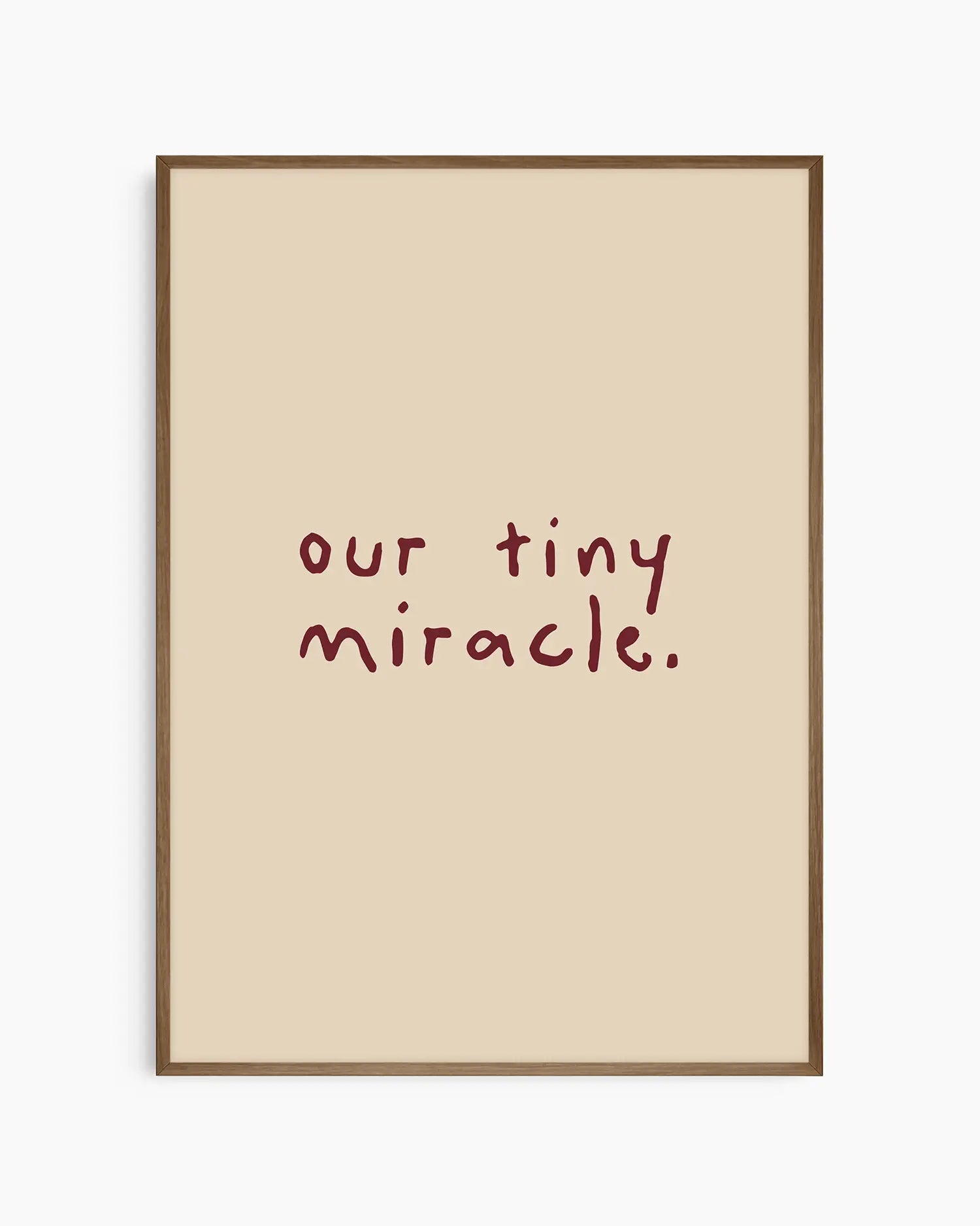 Barnrumstavla med orden "our tiny miracle." i vinröd handskriven typografi på beige bakgrund, inramad i en mörk ekram. En harmonisk och tidlös detalj till barnrummet.