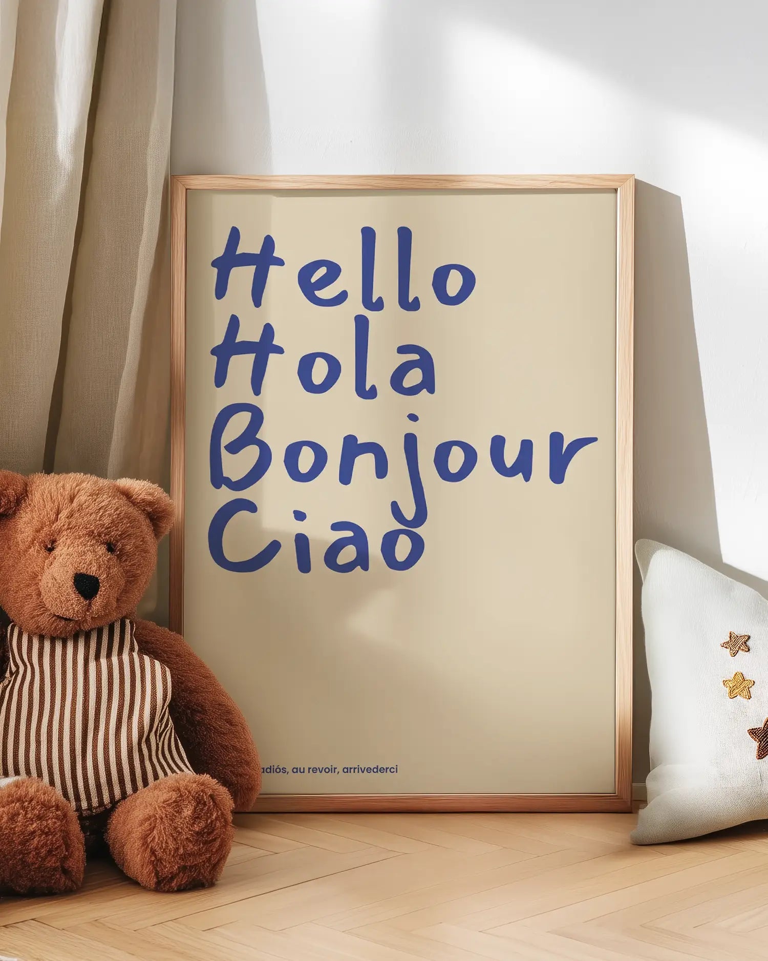Barntavla med texten “Hello Hola Bonjour Ciao” i blått på beige bakgrund lutad mot vägg bredvid nalle. En mjuk och vänlig väggdekoration som passar i barnrummet.