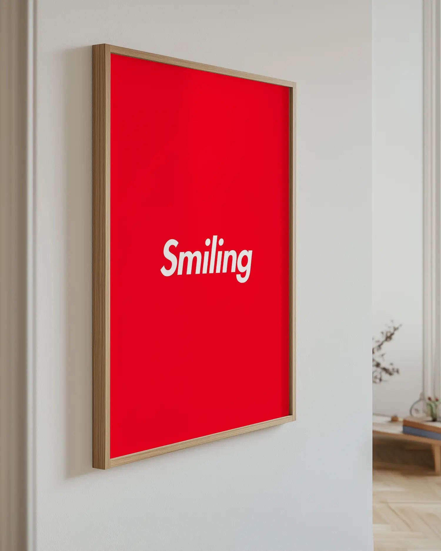Barntavla med vit text “Smiling” på röd bakgrund upphängd på vägg med ekram. En modern och livlig väggdekoration.