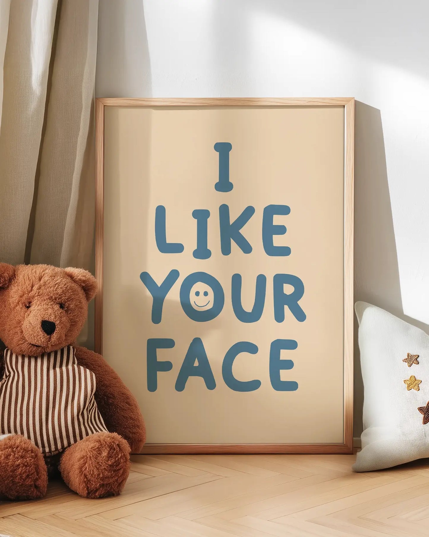 Barntavla med beige bakgrund och blå text “I LIKE YOUR FACE” med smiley lutad mot vägg bredvid nalle. En söt och positiv väggdekoration som passar perfekt i barnrummet.