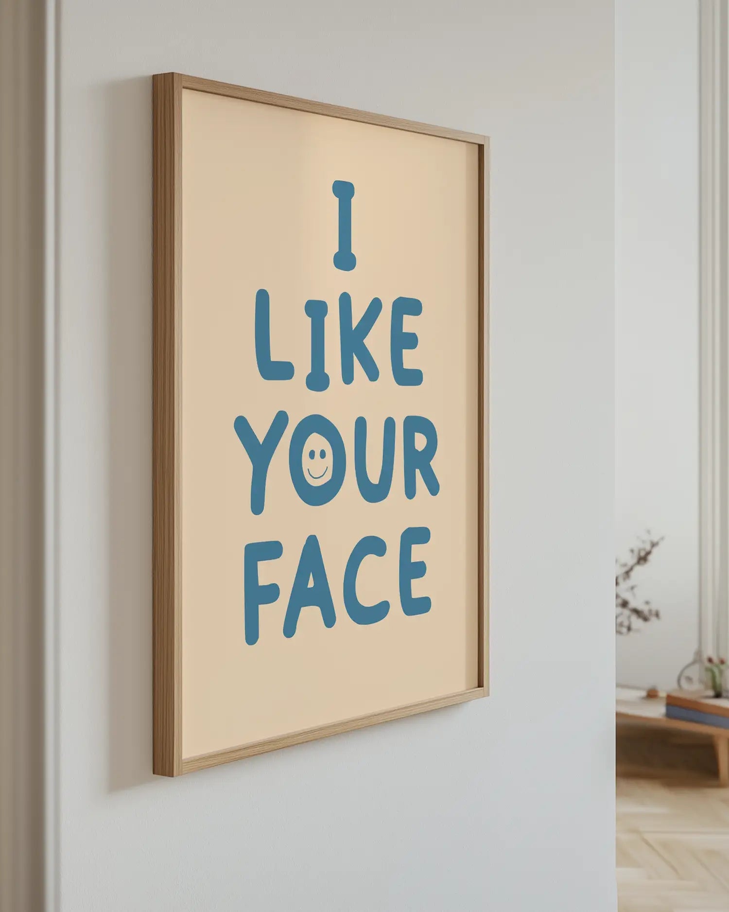 Barntavla med blå text “I LIKE YOUR FACE” på beige bakgrund upphängd på vägg med ekram. En modern och lekfull väggdekoration.