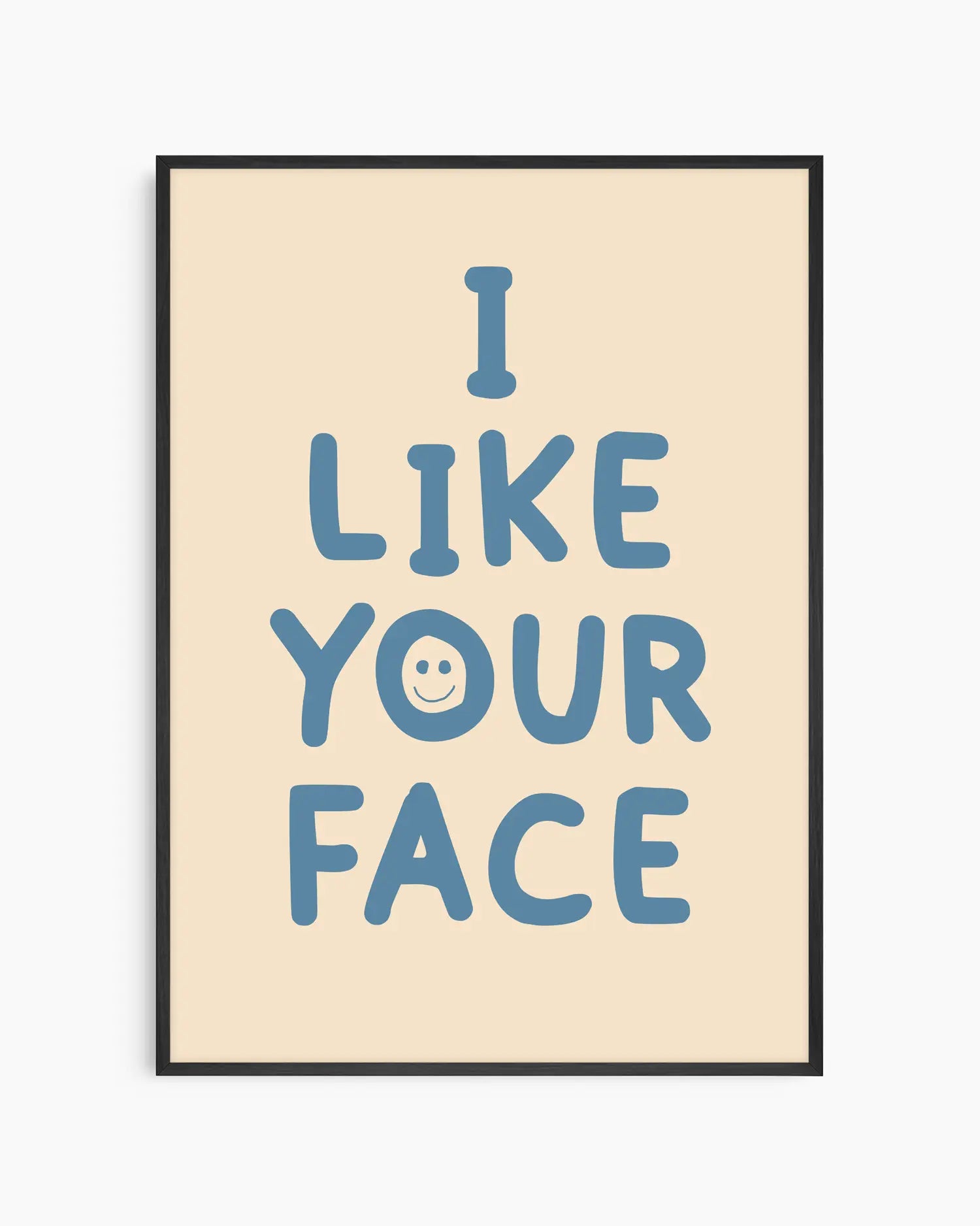 Barntavla med texten “I LIKE YOUR FACE” i blått med ett litet smiley-ansikte på beige bakgrund, inramad i svart träram. En glad och lekfull väggdekoration.