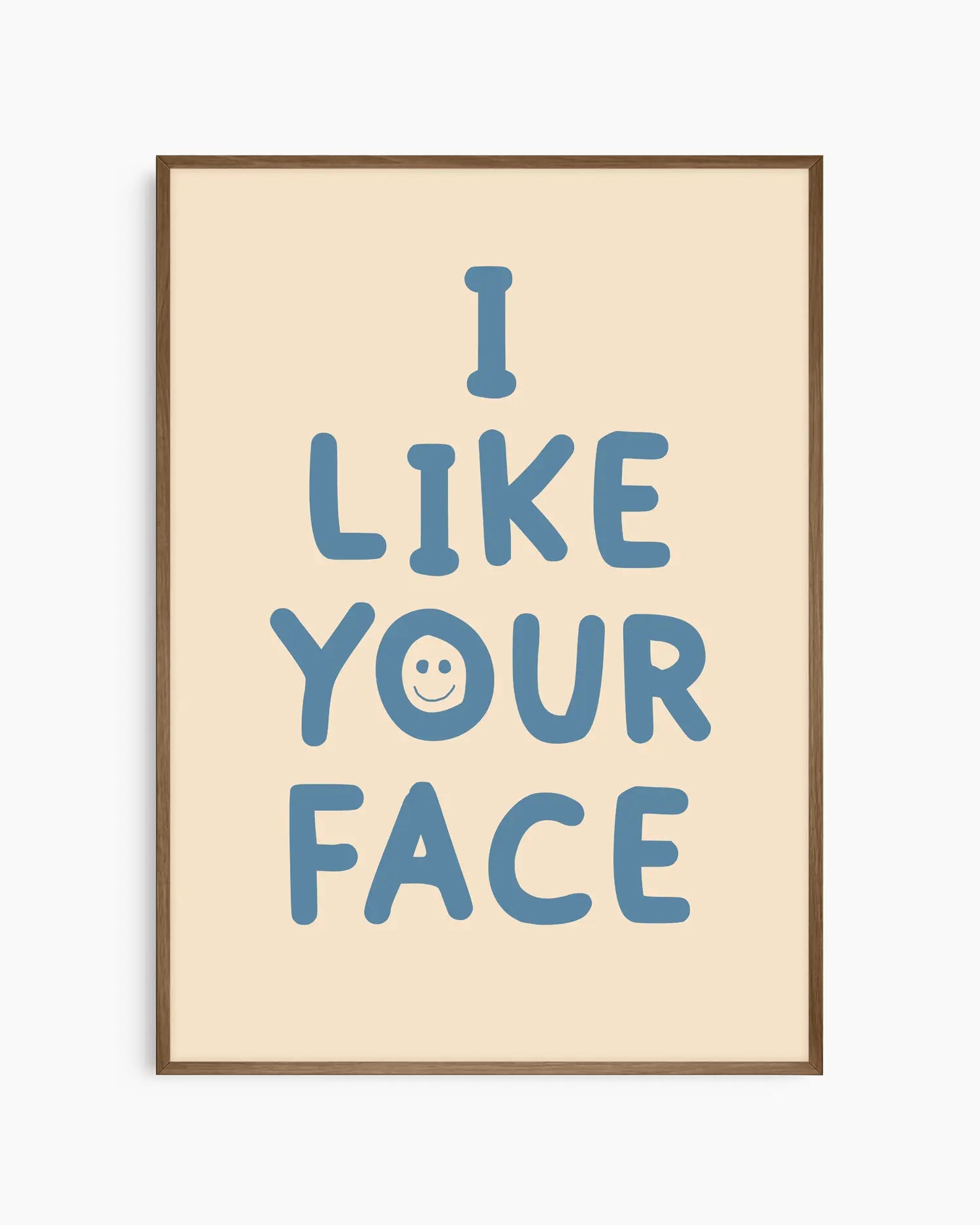 Barntavla med beige bakgrund och blå text “I LIKE YOUR FACE” med smiley, inramad i träram i mörk ek. En charmig och humoristisk väggdekoration med retrokänsla.