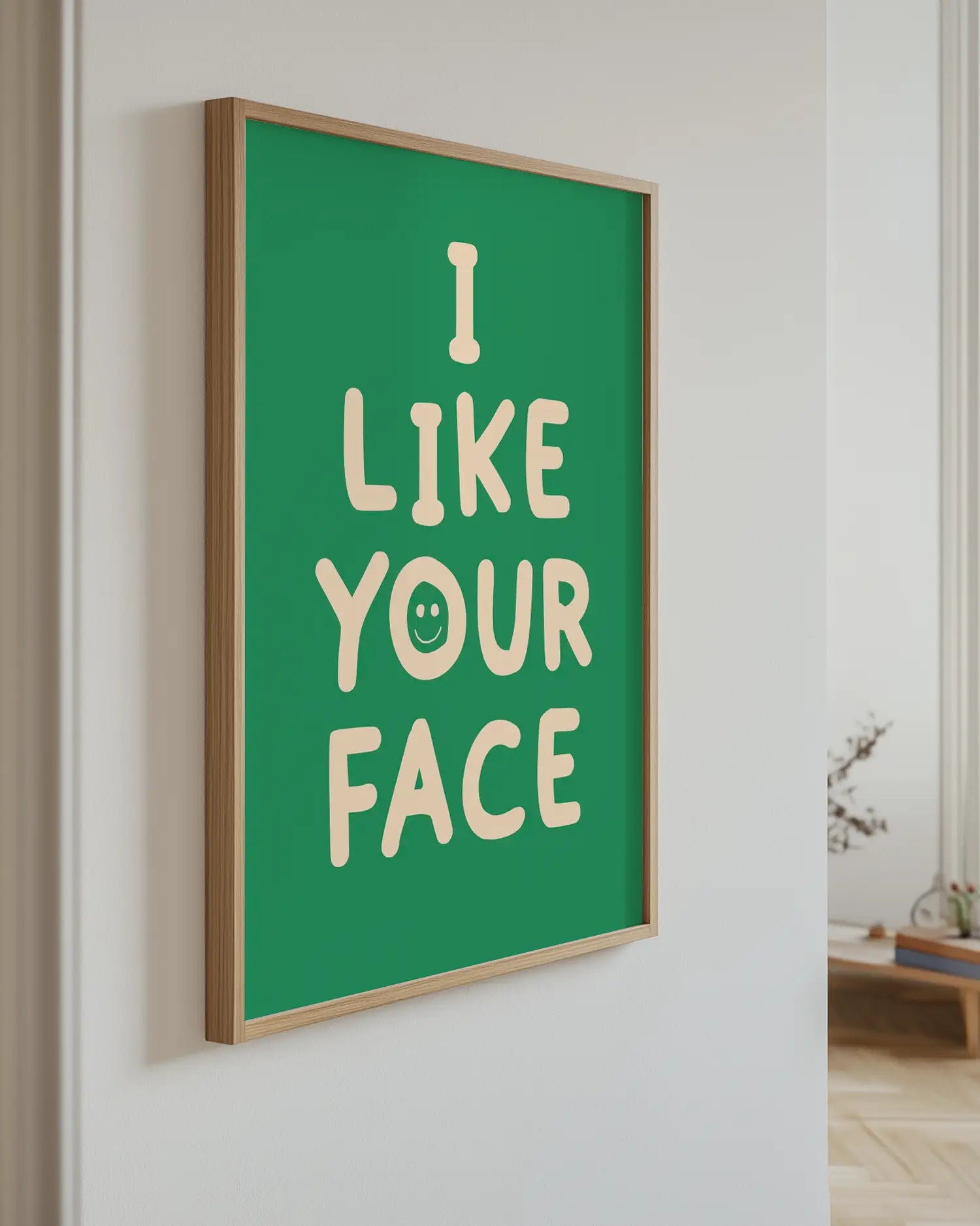 Barntavla med texten “I LIKE YOUR FACE” i beige på grön bakgrund upphängd på vägg med ekram. En lekfull och kärleksfull dekoration.