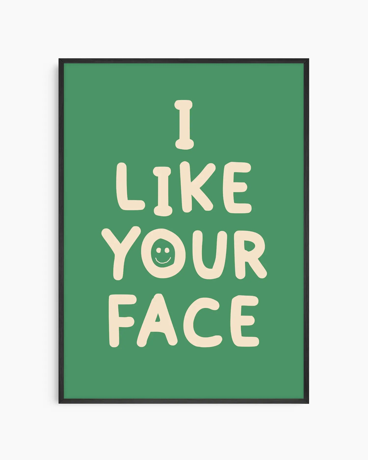 Barntavla med texten “I LIKE YOUR FACE” i ljus beige färg med ett litet smiley-ansikte på grön bakgrund, inramad i svart träram. En glad och lekfull väggdekoration.