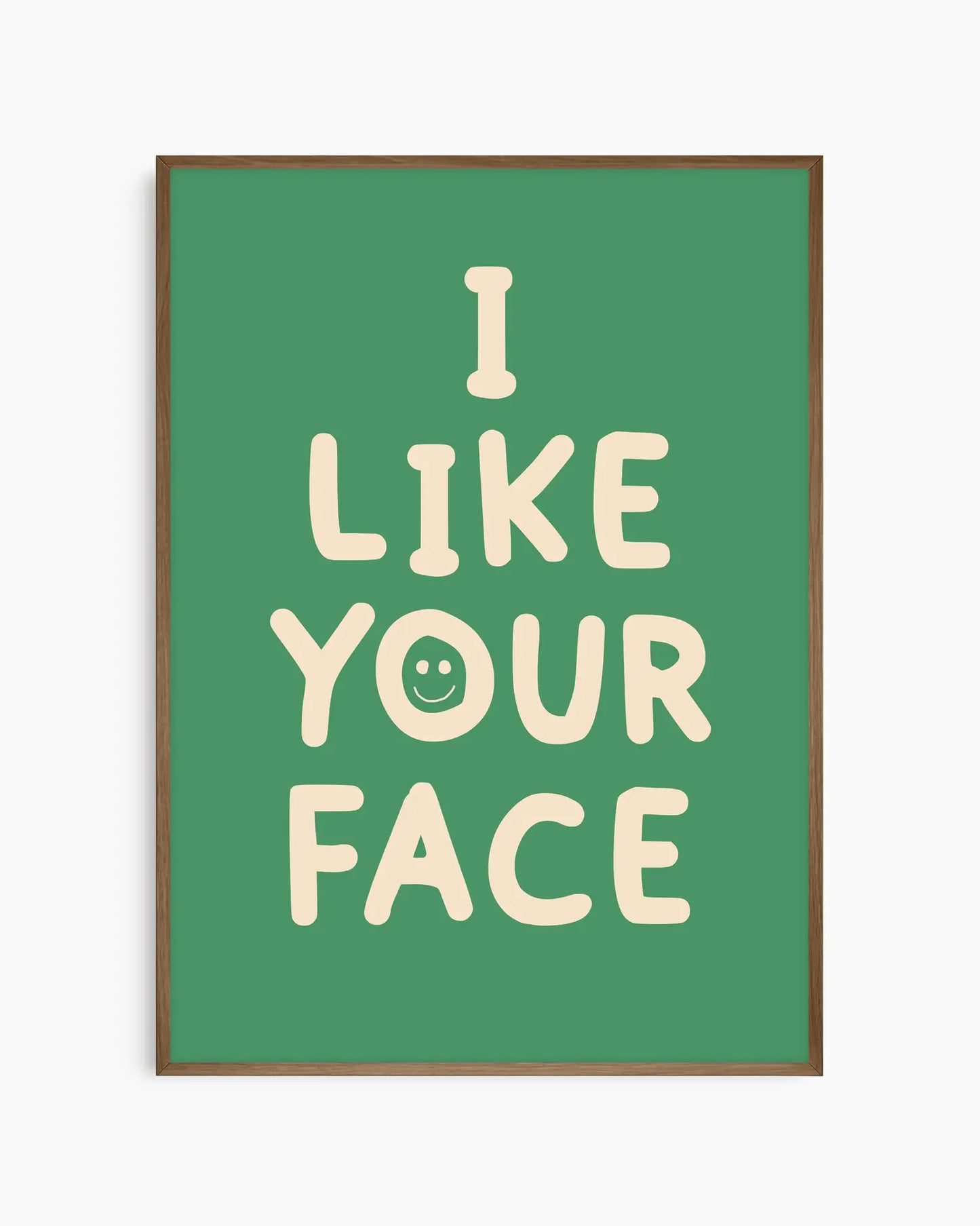Barntavla med beige text “I LIKE YOUR FACE” och smiley på grön bakgrund, inramad i träram i mörk ek. En varm och charmig väggdekoration med humoristisk ton.