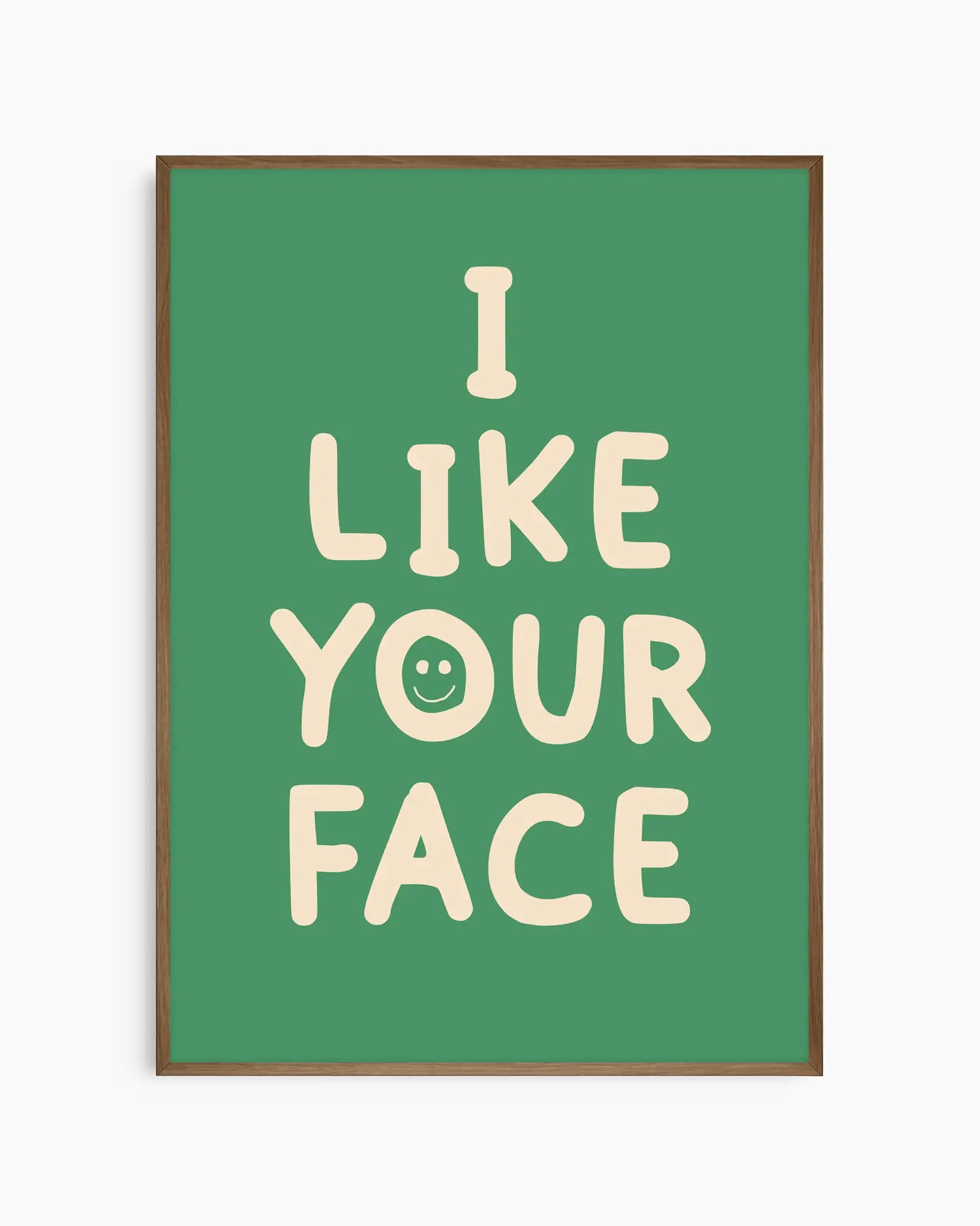 Barntavla med beige text “I LIKE YOUR FACE” och smiley på grön bakgrund, inramad i träram i mörk ek. En varm och charmig väggdekoration med humoristisk ton.