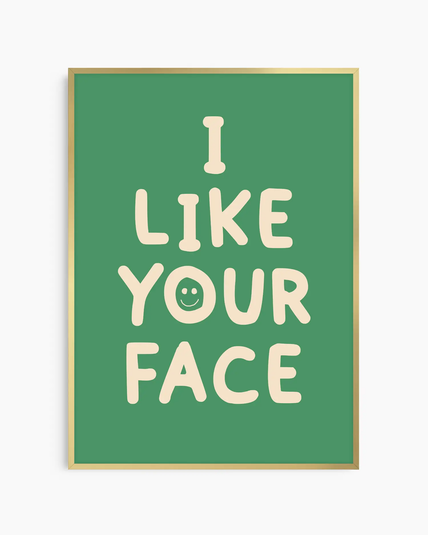 Barntavla med grön bakgrund och beige text “I LIKE YOUR FACE” med smiley, inramad i guld aluminiumram. En positiv och lekfull väggdekoration som sprider glädje.