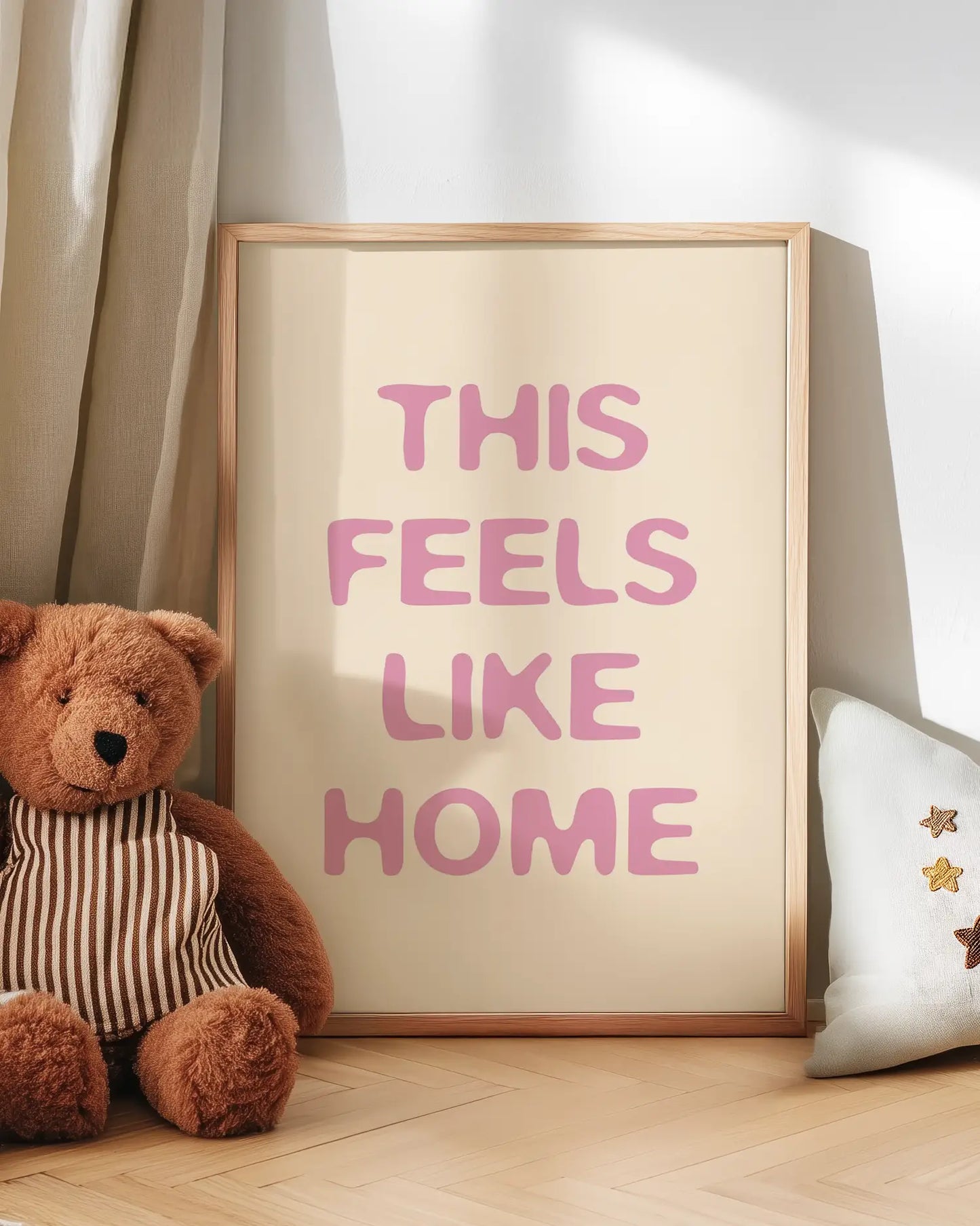 Barntavla med texten “This Feels Like Home” i rosa ton lutad mot vägg bredvid nalle. En söt och trygg väggdekoration som skapar hemtrevnad.