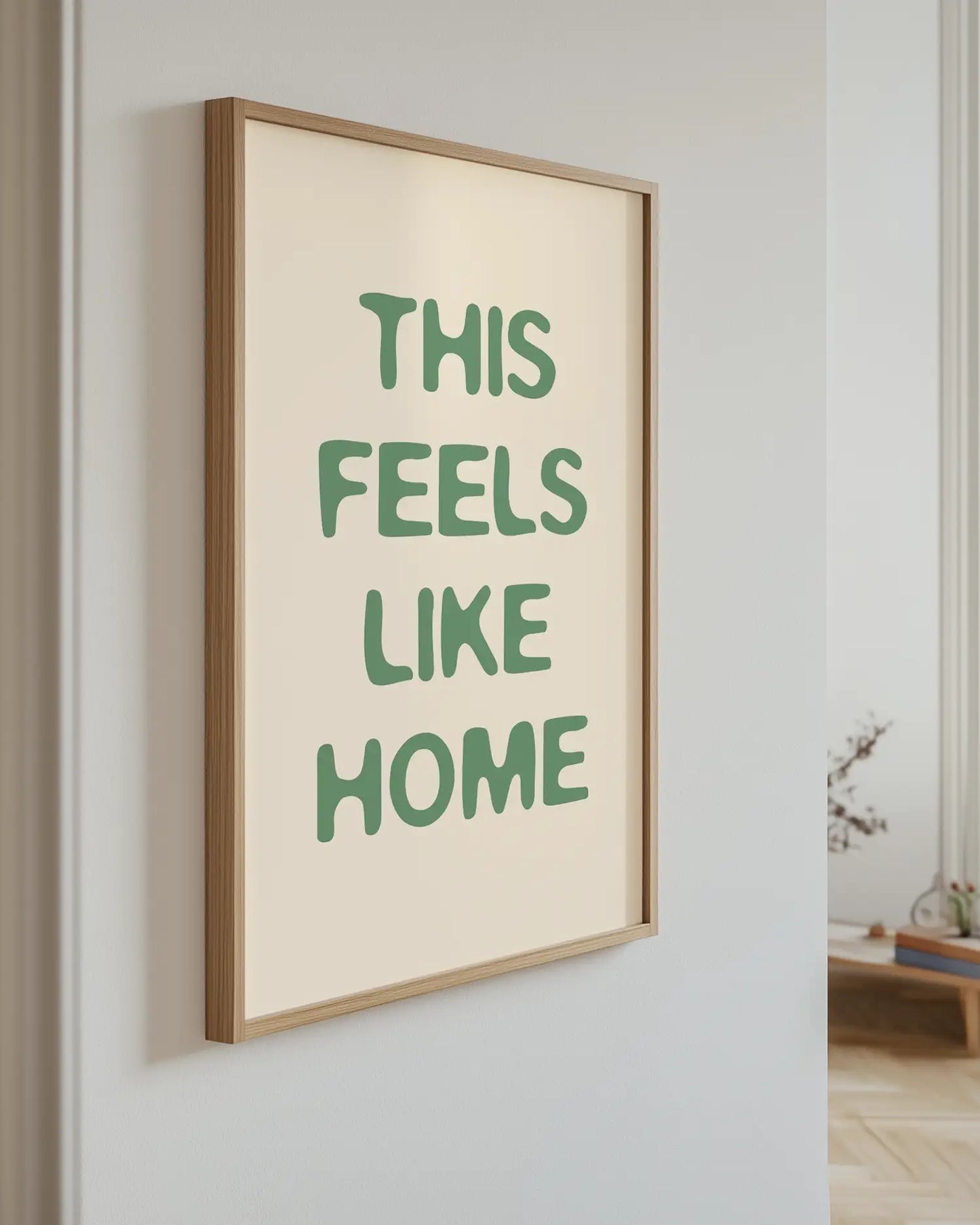 Barntavla med grön text “This Feels Like Home” upphängd på vägg med ekram. En stilren och mysig dekoration som passar perfekt i barnrummet.