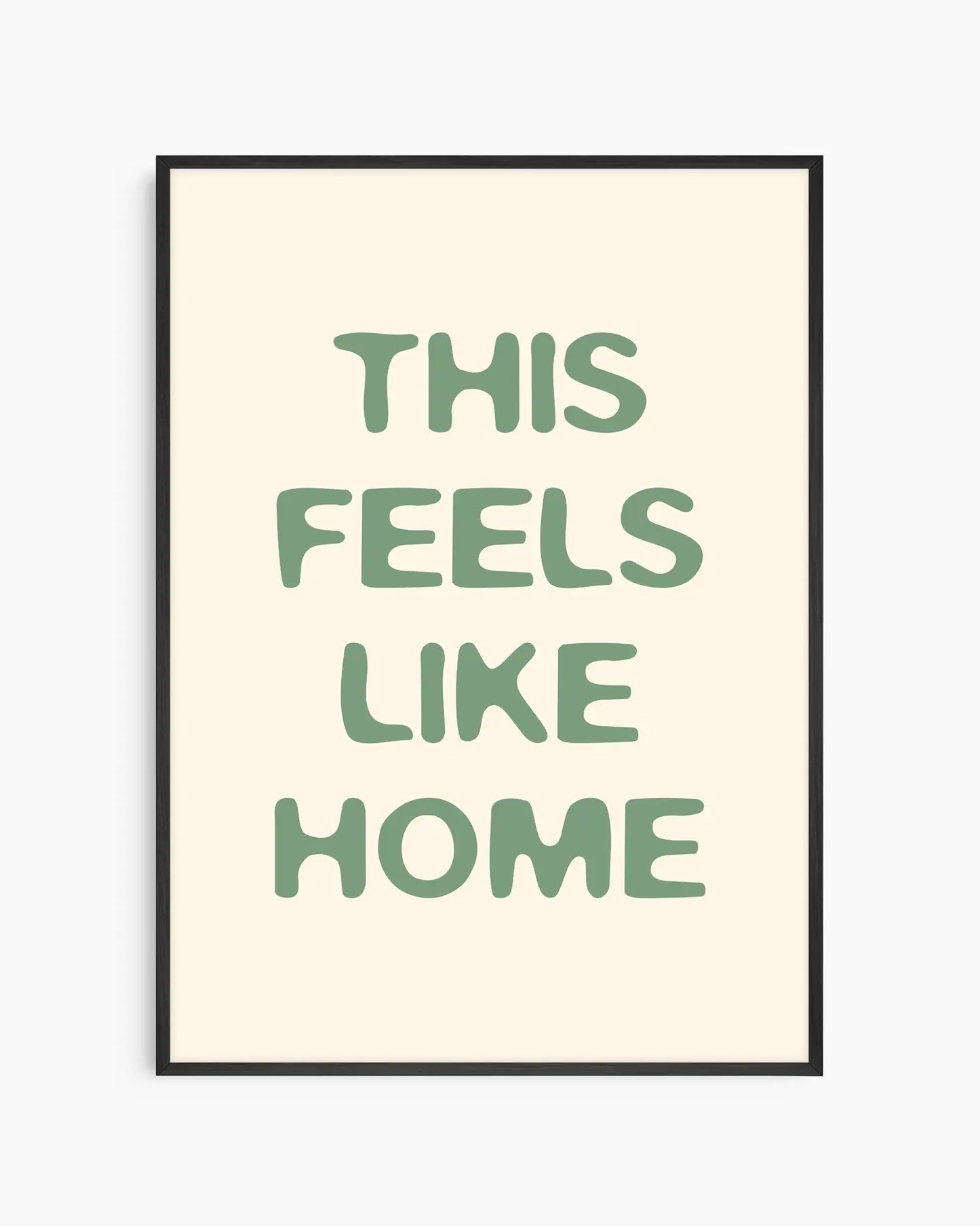 Barntavla med texten “This Feels Like Home” i mjuk grön typografi på ljus bakgrund, inramad i svart träram. En varm och harmonisk väggdekoration med hemtrevlig känsla.