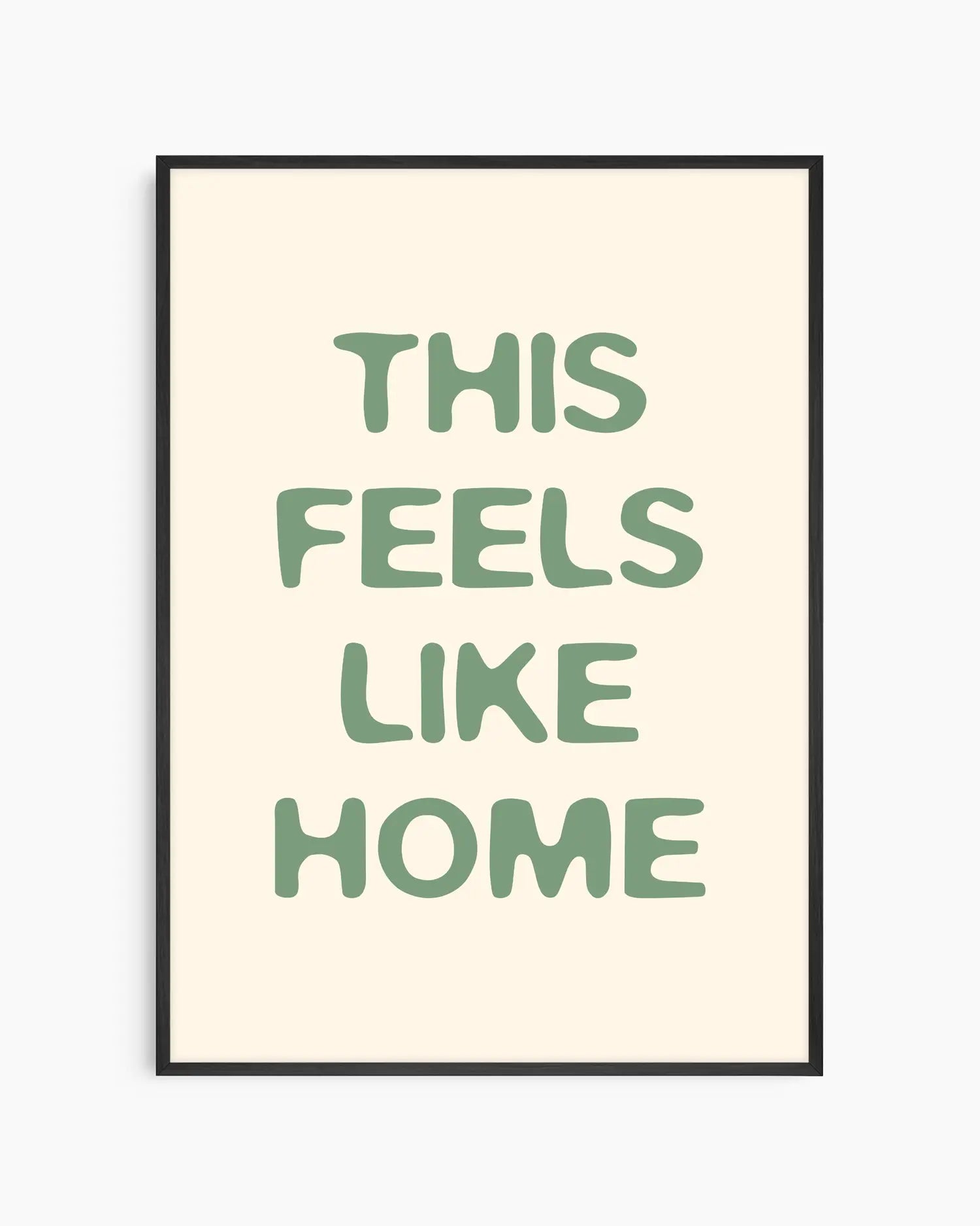 Barntavla med texten “This Feels Like Home” i mjuk grön typografi på ljus bakgrund, inramad i svart träram. En varm och harmonisk väggdekoration med hemtrevlig känsla.