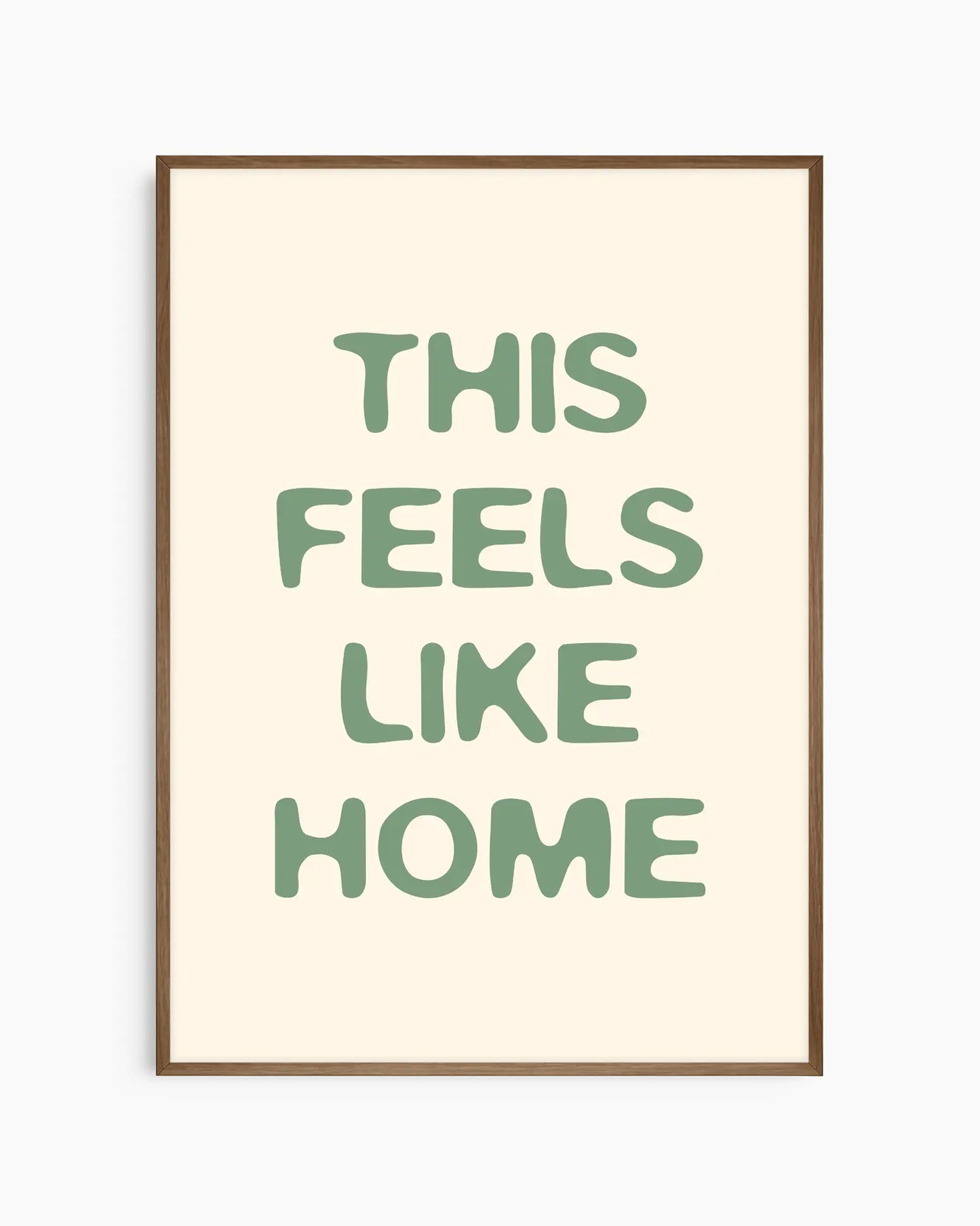 Barntavla med grön text “This Feels Like Home” på beige bakgrund, inramad i träram i mörk ek. En tidlös och lugn väggdekoration som skapar trygg stämning.