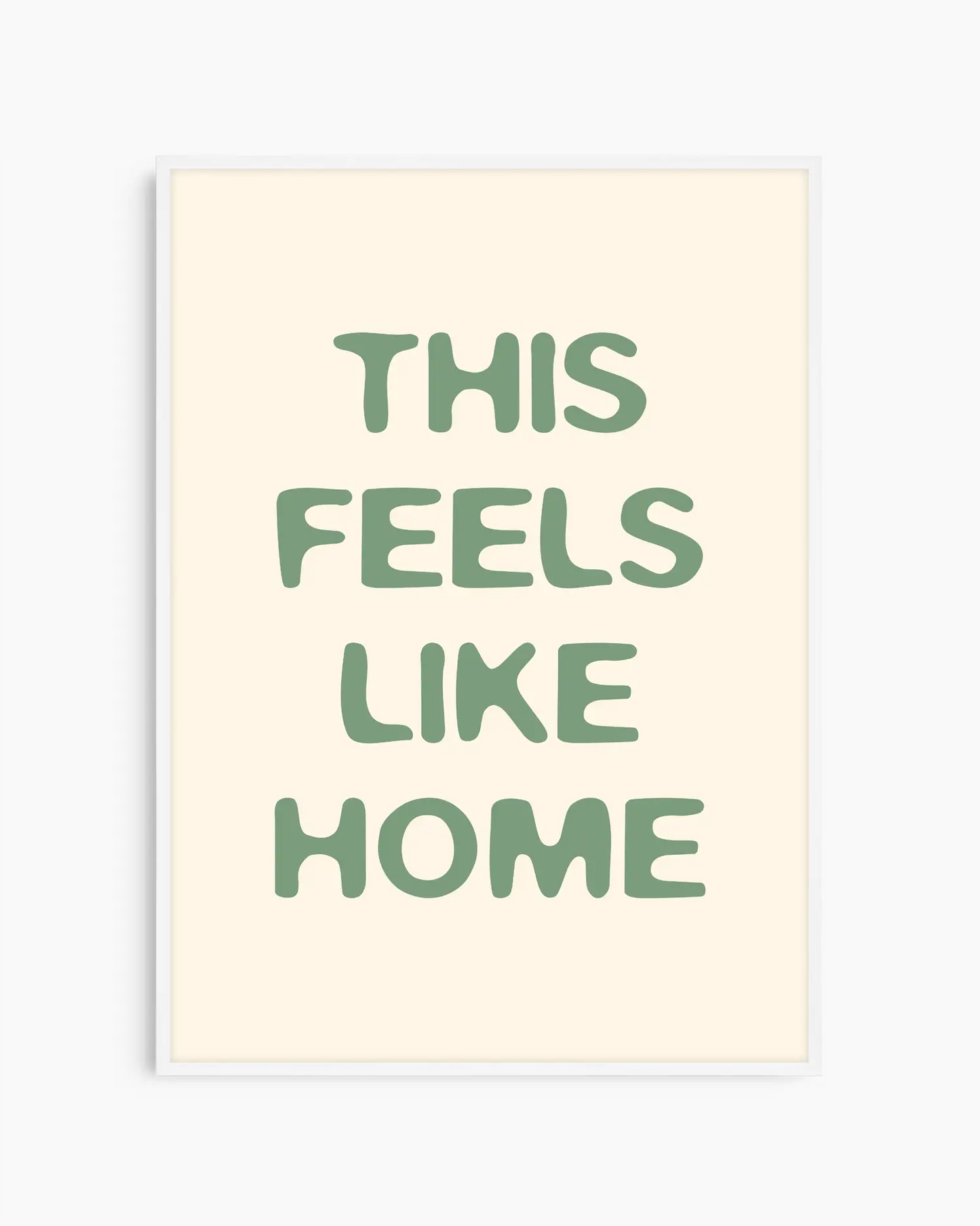 Barntavla med grön text “This Feels Like Home” på beige bakgrund, inramad i vit träram. En ljus och enkel väggdekoration som passar perfekt i barnrum.