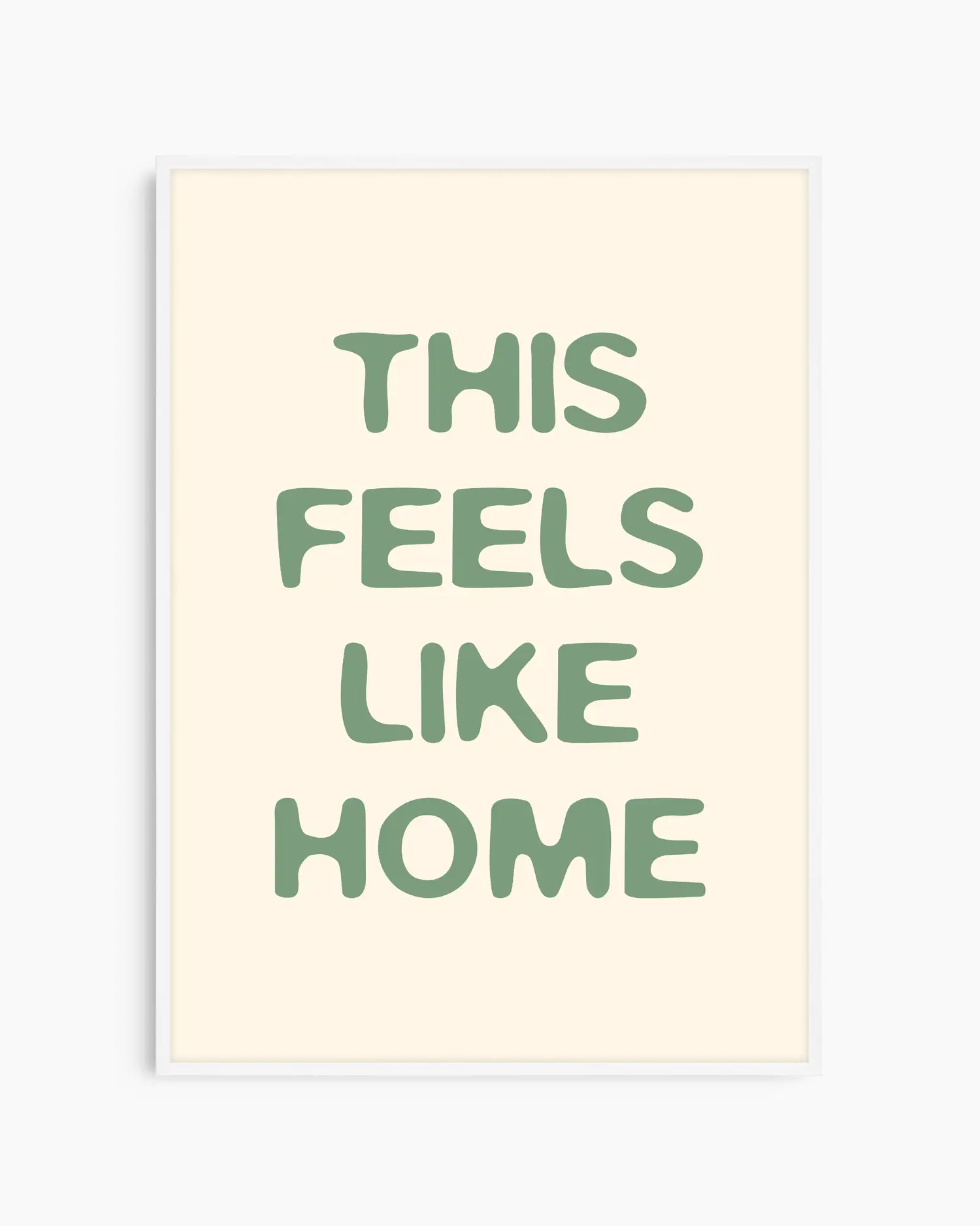 Barntavla med grön text “This Feels Like Home” på beige bakgrund, inramad i vit träram. En ljus och enkel väggdekoration som passar perfekt i barnrum.