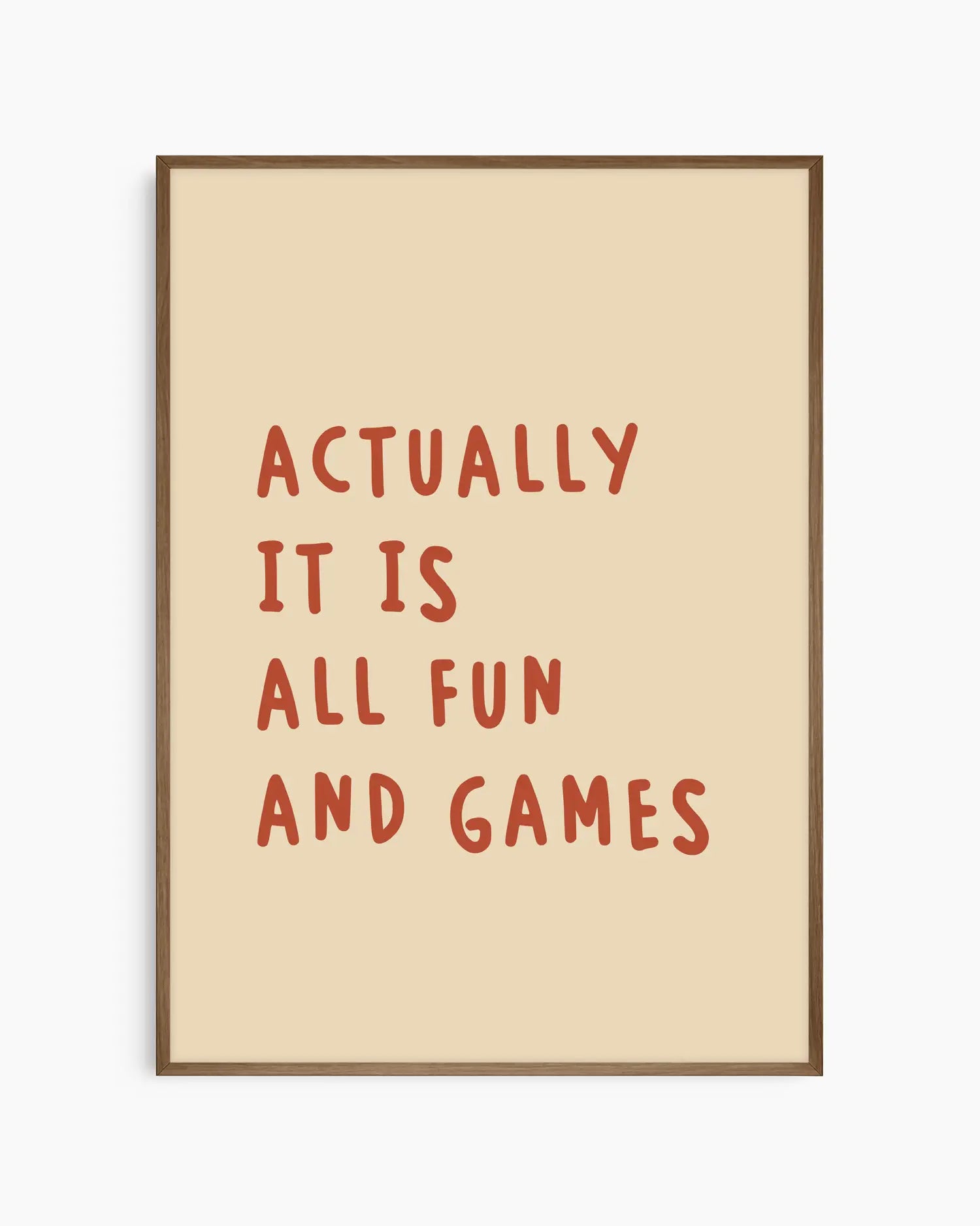 Barntavla med rödbrun text “ACTUALLY IT IS ALL FUN AND GAMES” på varm beige bakgrund, inramad i träram i mörk ek. En stilren och varm detalj till barnrummet.