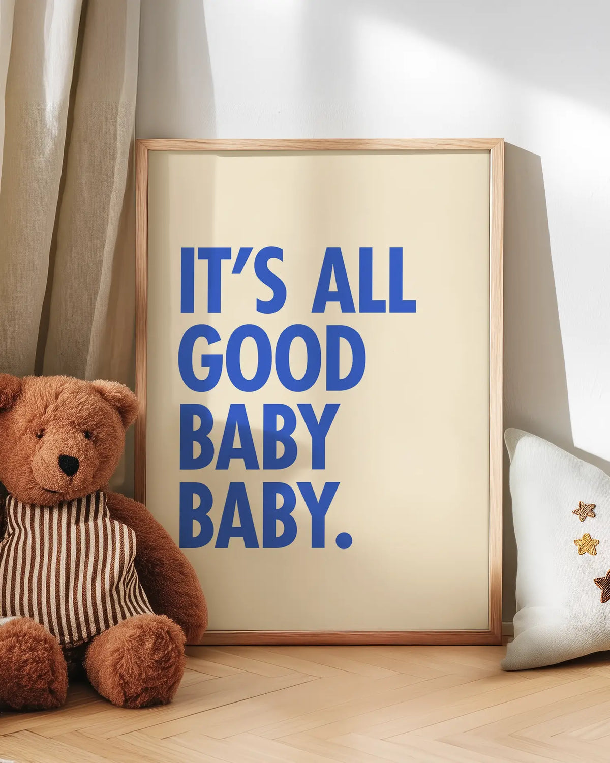 Barntavla med texten "IT’S ALL GOOD BABY BABY." lutad mot vägg bredvid nalle. En charmig och lugn scen med en positiv känsla.