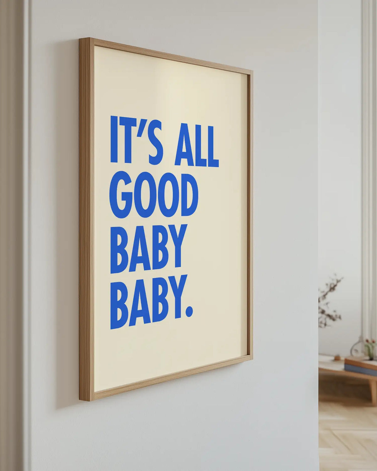 Barntavla med texten "IT’S ALL GOOD BABY BABY." i blå text på ljus bakgrund, upphängd på vägg med ekram. En fräsch och trendig väggdetalj.