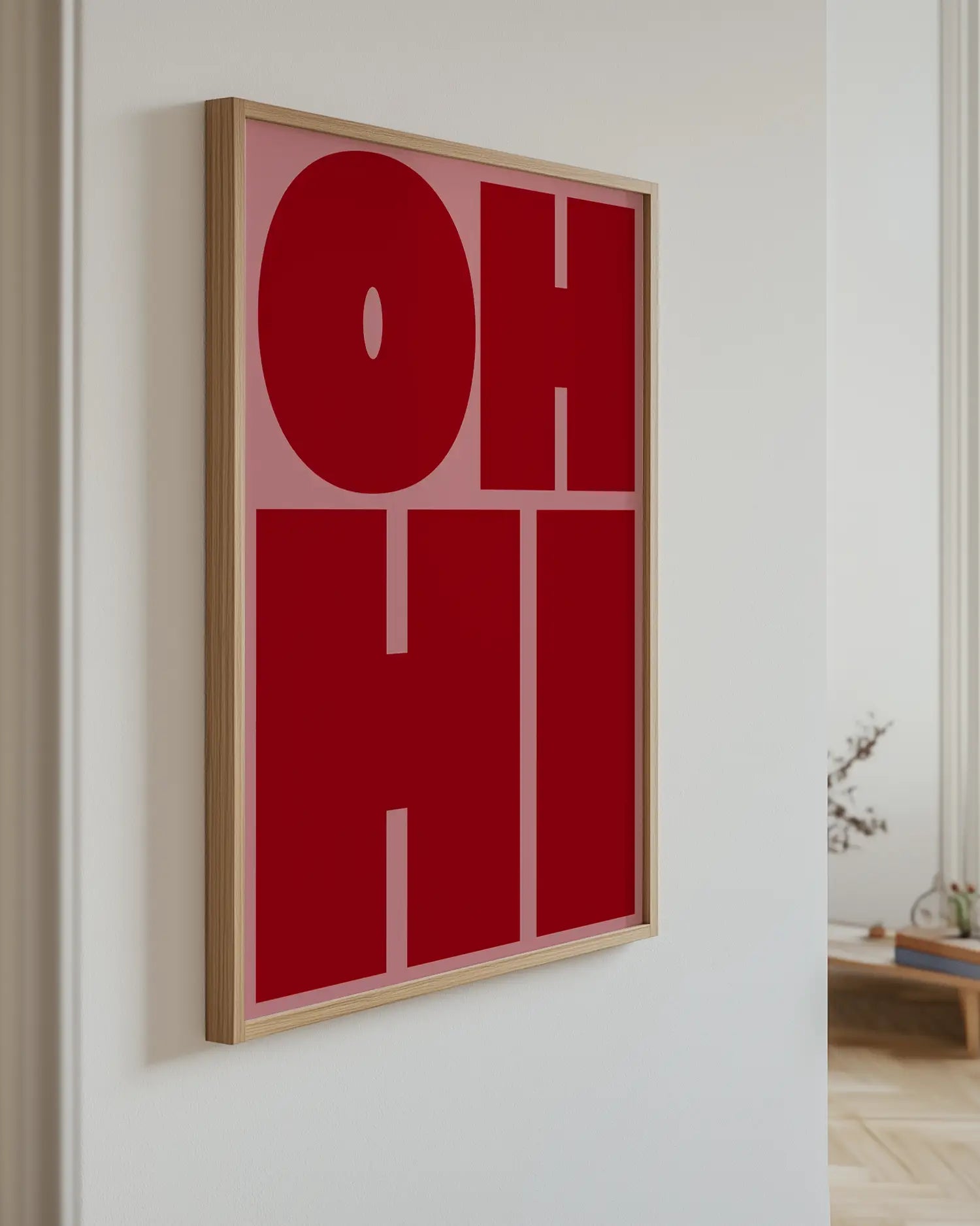 Barntavla med texten "OH HI" i mörkröd text på rosa bakgrund, upphängd på vägg med ekram. En modern och färgstark detalj som väcker uppmärksamhet.