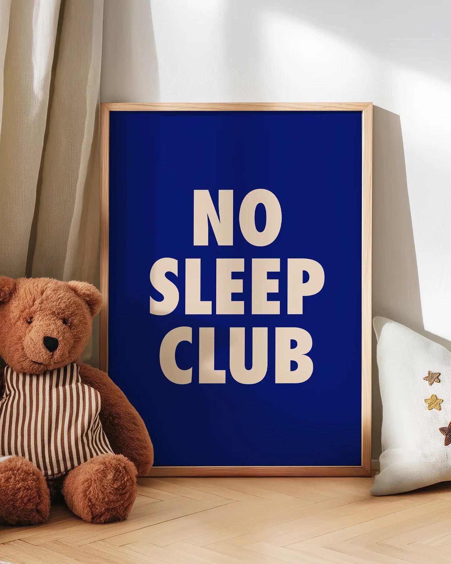 Barntavla med texten "No Sleep Club" i ljusrosa mot mörkblå bakgrund, lutad mot vägg bredvid nalle. En lekfull och mysig scen i barnrummet.