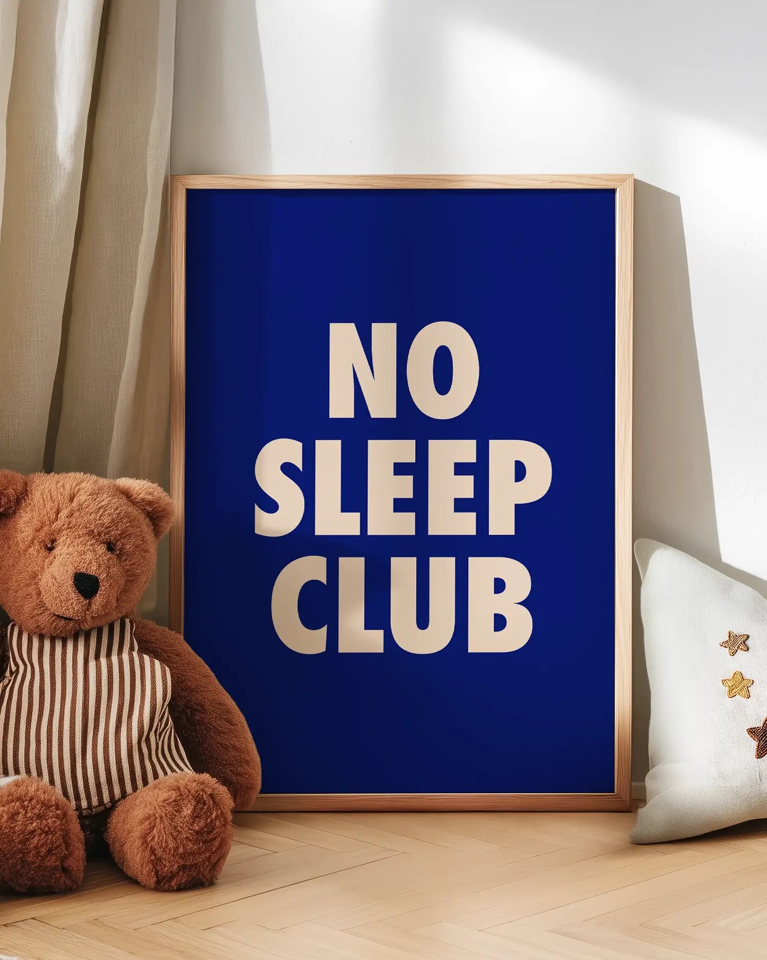 Barntavla med texten "No Sleep Club" i ljusrosa mot mörkblå bakgrund, lutad mot vägg bredvid nalle. En lekfull och mysig scen i barnrummet.