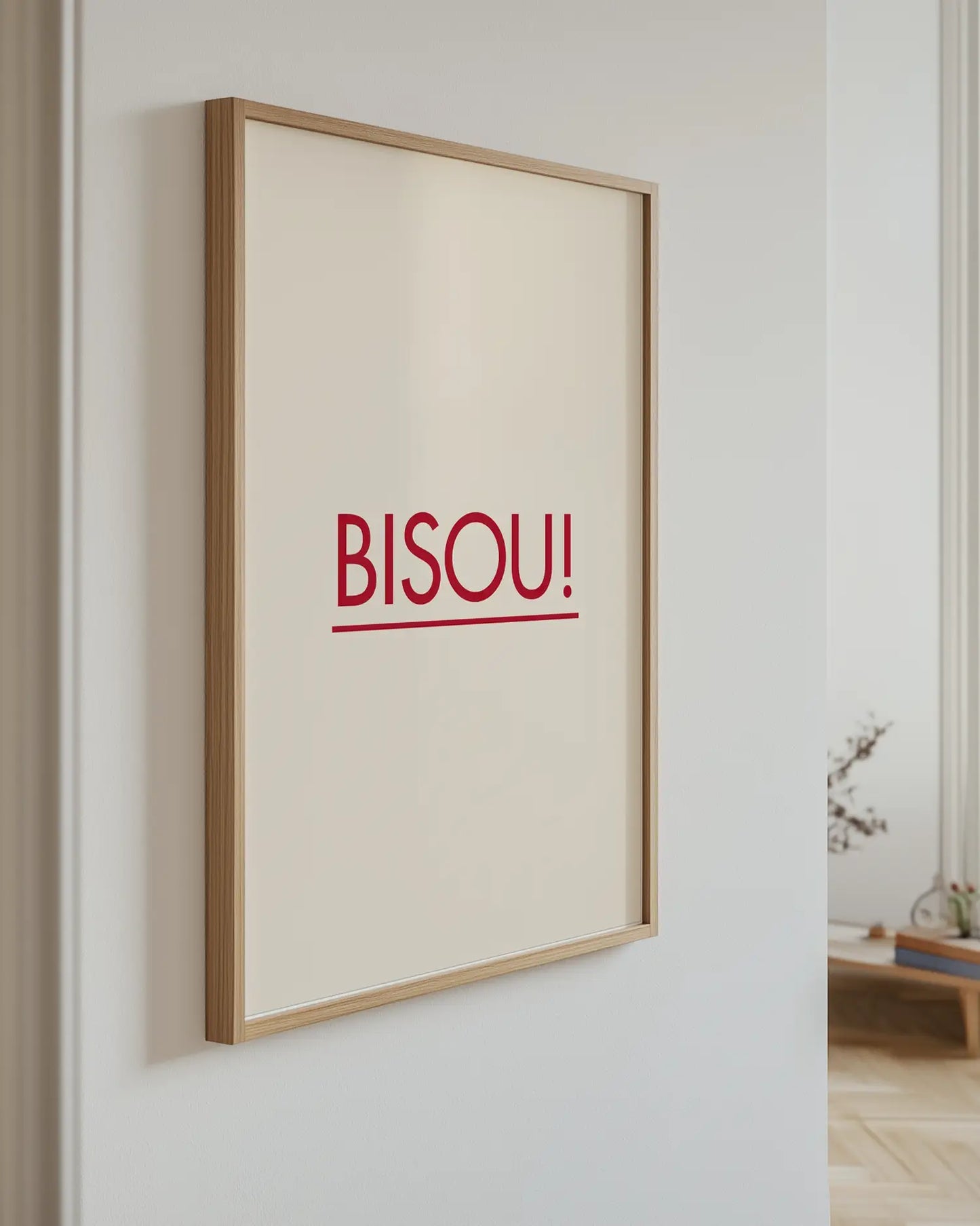 Barntavla med texten "BISOU!" i rött mot beige bakgrund, upphängd på vägg med ekram. En modern och elegant detalj som sprider värme och glädje.