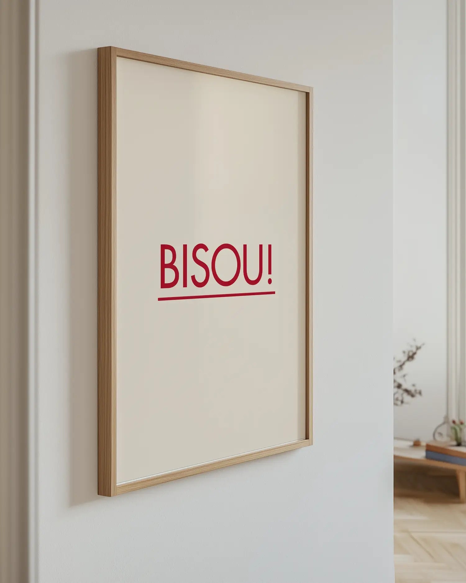 Barntavla med texten "BISOU!" i rött mot beige bakgrund, upphängd på vägg med ekram. En modern och elegant detalj som sprider värme och glädje.