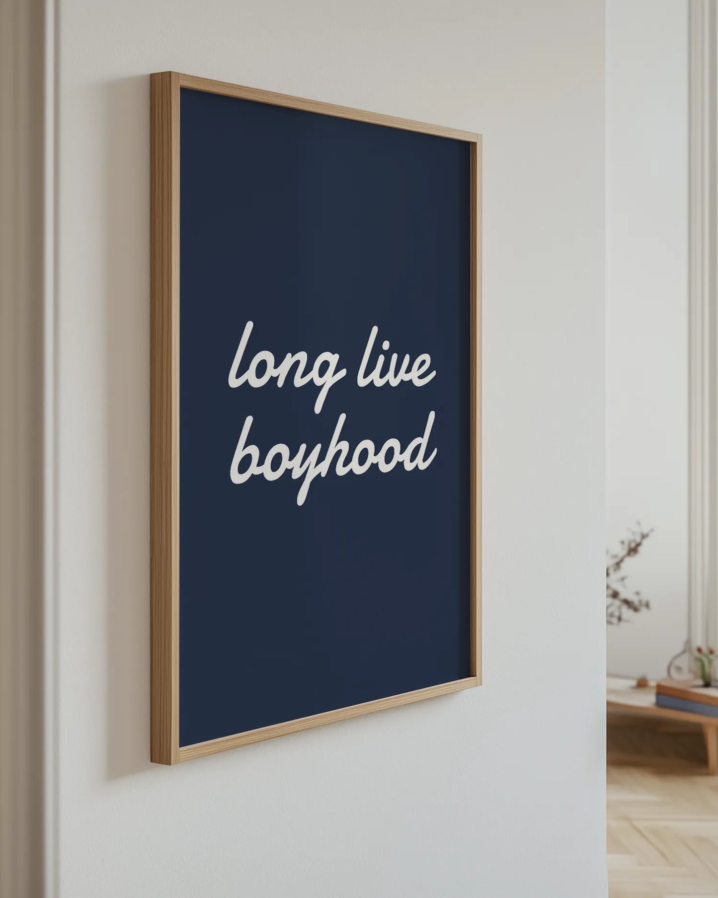 "Long live boyhood"-poster i ekram hängande på ljus vägg i ett modernt hem. Den blå textpostern med vit handskriven stil skapar en harmonisk och personlig känsla i barnrum, lekrum eller familjehem.
