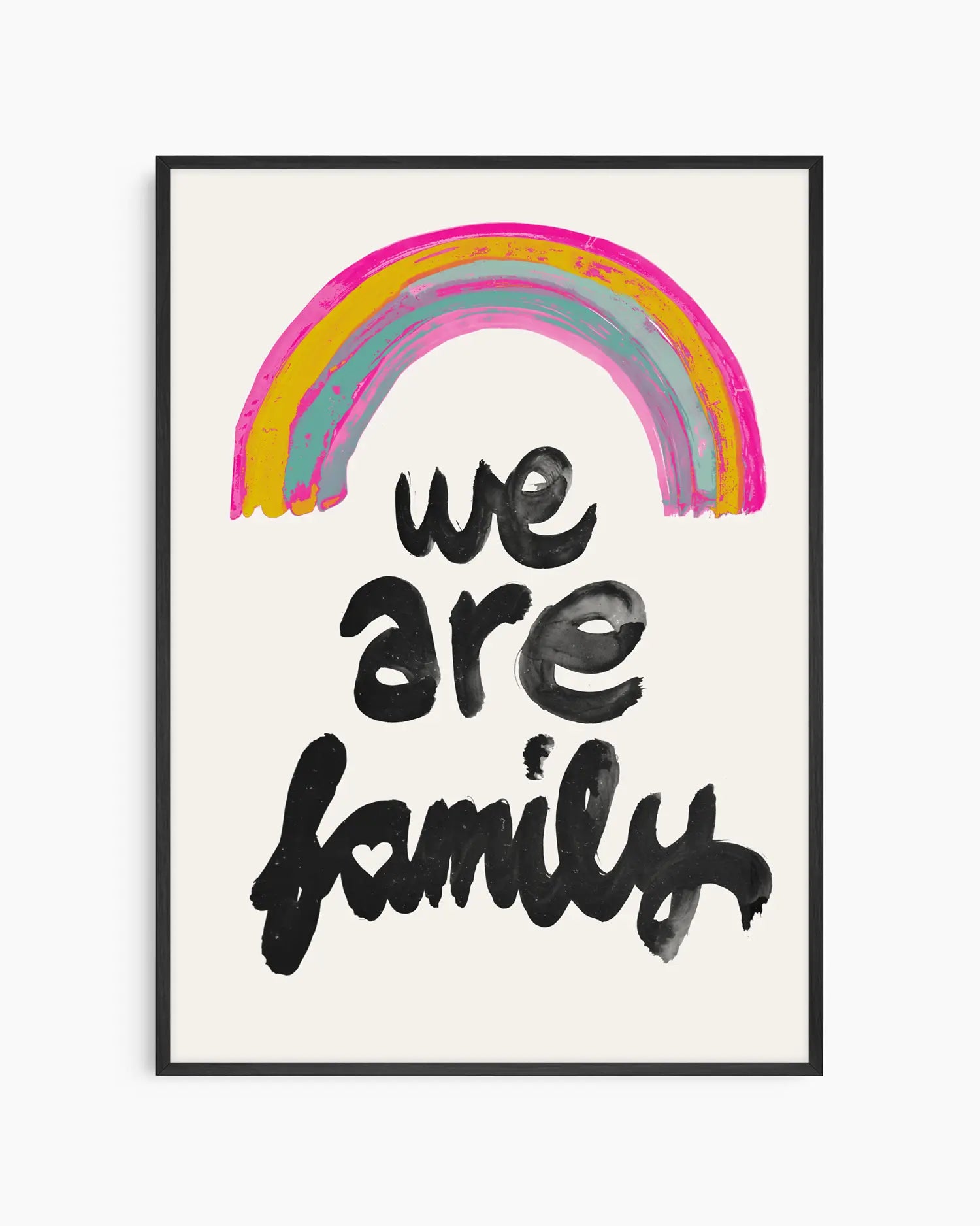 Barntavla med handmålad regnbåge i rosa, gult och turkost ovanför texten "WE ARE FAMILY" i svart penselstil, inramad i svart träram som ger en modern och varm känsla i barnrummet.