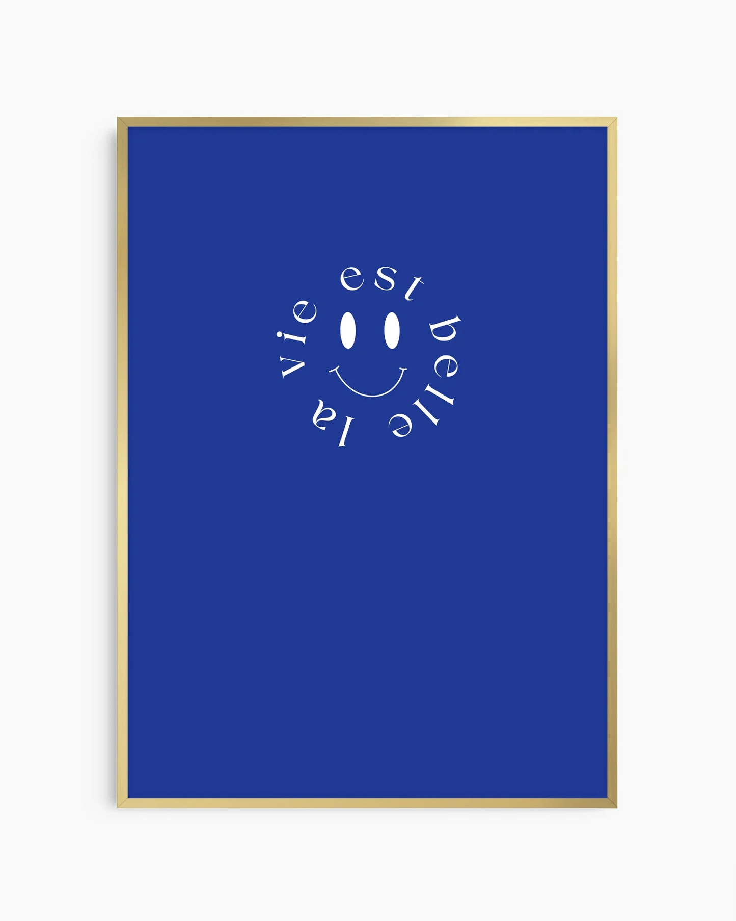 Barntavla med vit smiley och frasen ”la vie est belle”, inramad i guld aluminiumram som ger motivet en lyxig kontrast mot den blå bakgrunden.