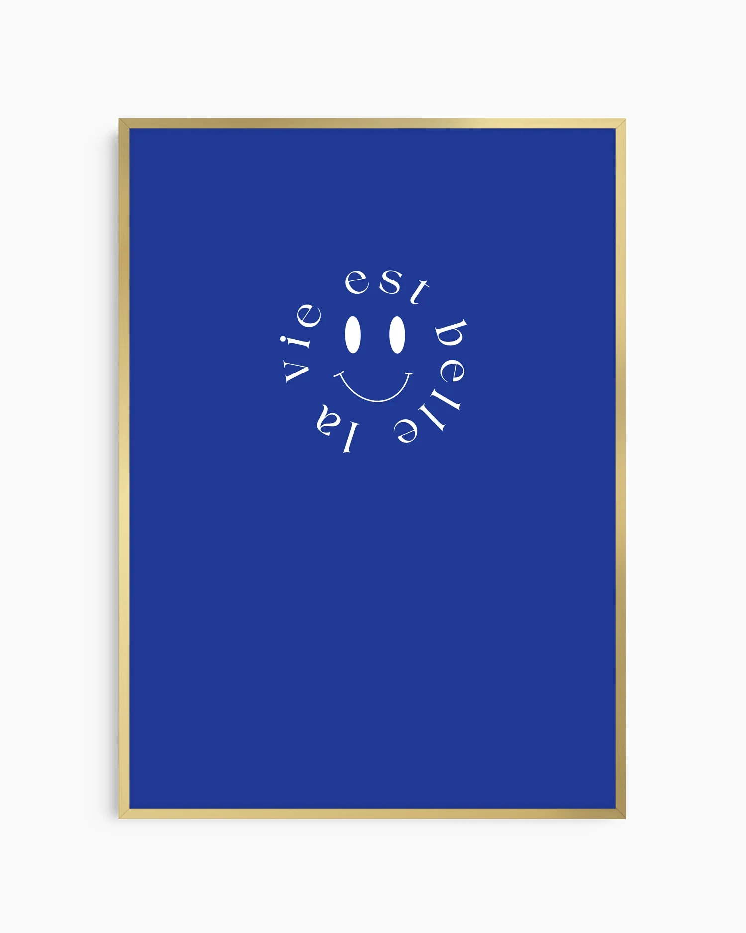 Barntavla med vit smiley och frasen ”la vie est belle”, inramad i guld aluminiumram som ger motivet en lyxig kontrast mot den blå bakgrunden.