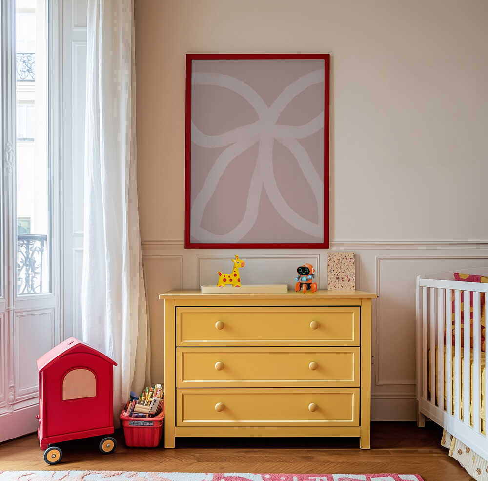 Inramad barntavla med rosa abstrakta linjer ovanför den gula byrån och skapar en mjuk och kreativ stämning i barnrummet.