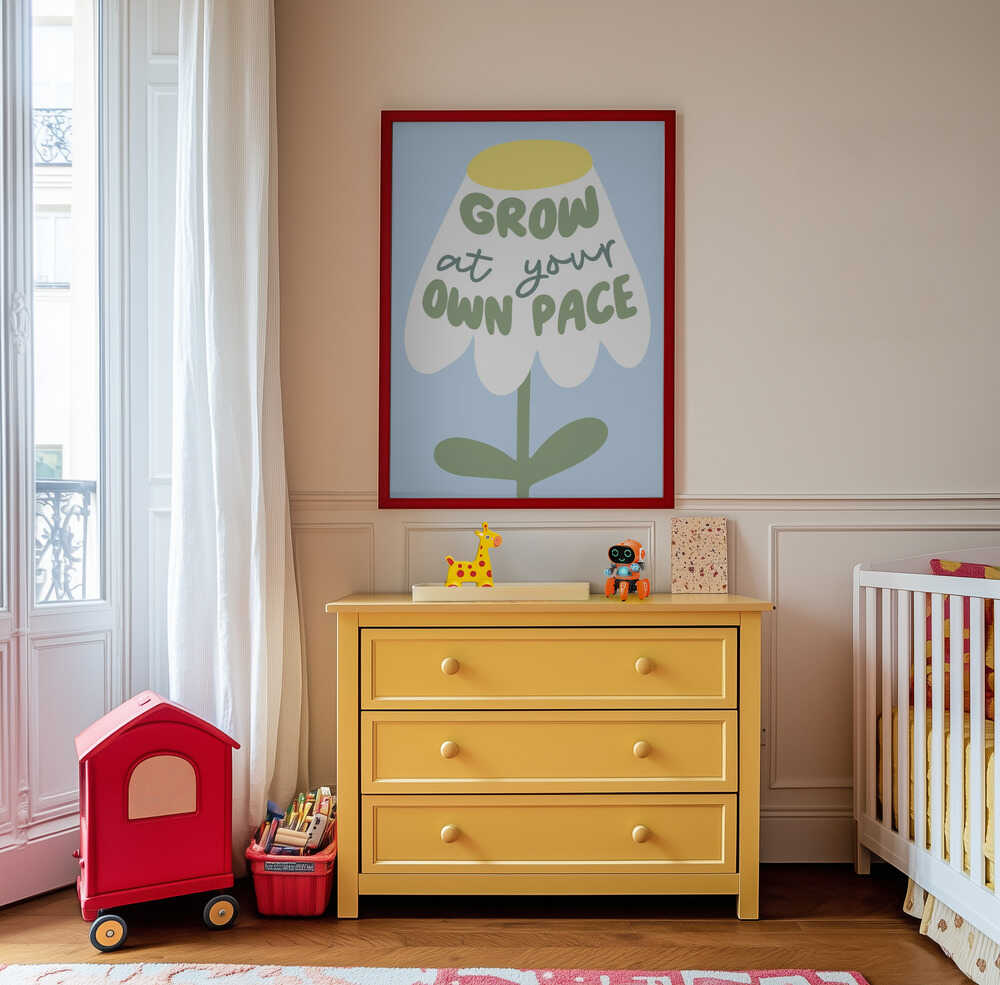 Inramad barntavla med blomillustration och texten "GROW AT YOUR OWN PACE" placerad ovanför en gul byrå i ett barnrum. En färgglad och uppmuntrande detalj.