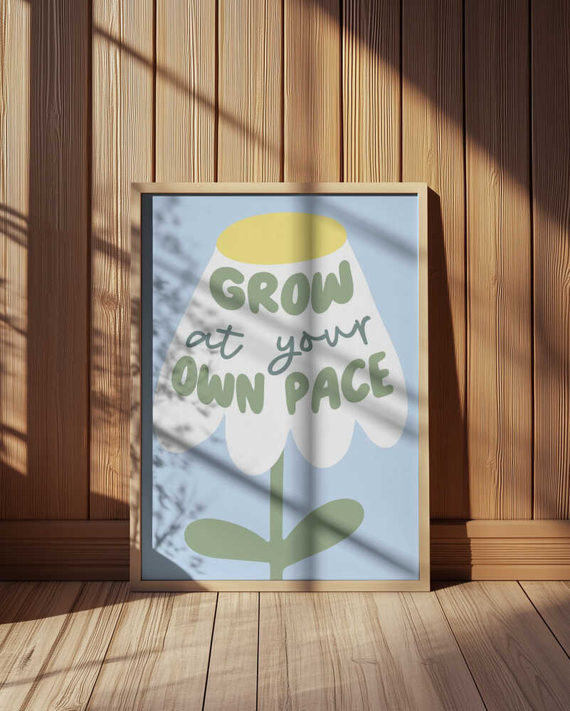 Inramad barntavla med budskapet "GROW AT YOUR OWN PACE" placerad på golvet i barnrum med träpanelvägg. En harmonisk och naturlig stil.